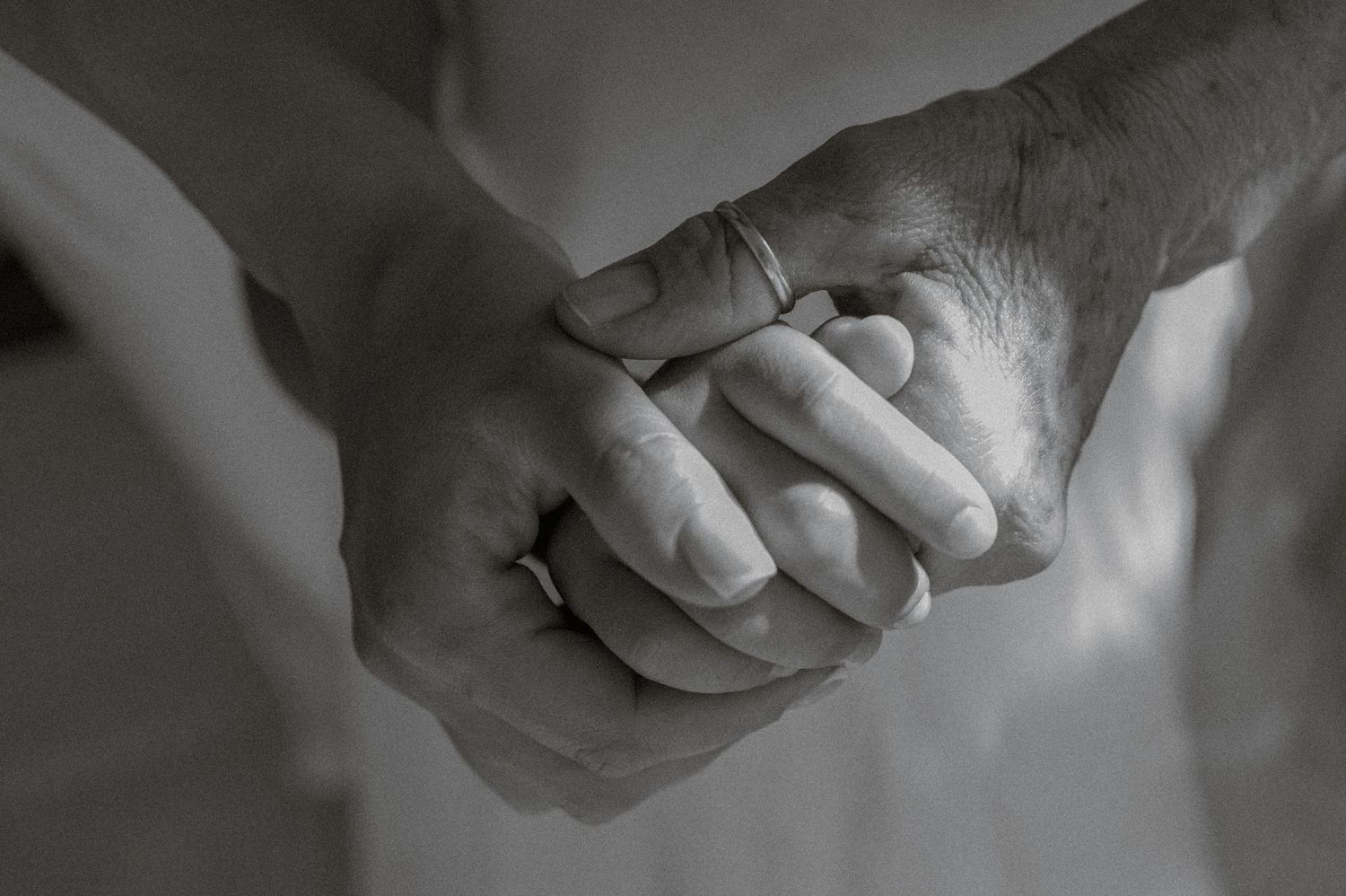 Black and white close-up of three people clasping hands with a wedding ring visible, representing family and unity.