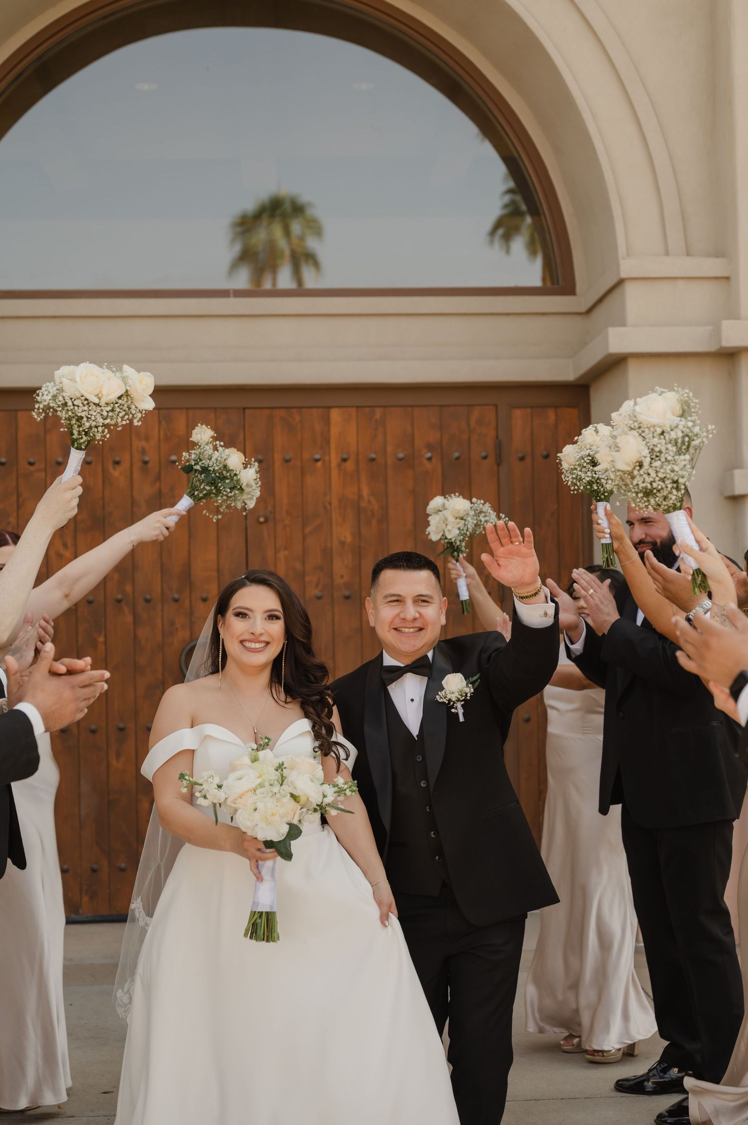 Bride and groom joyfully exit ceremony as guests cheer and toss flower petals.