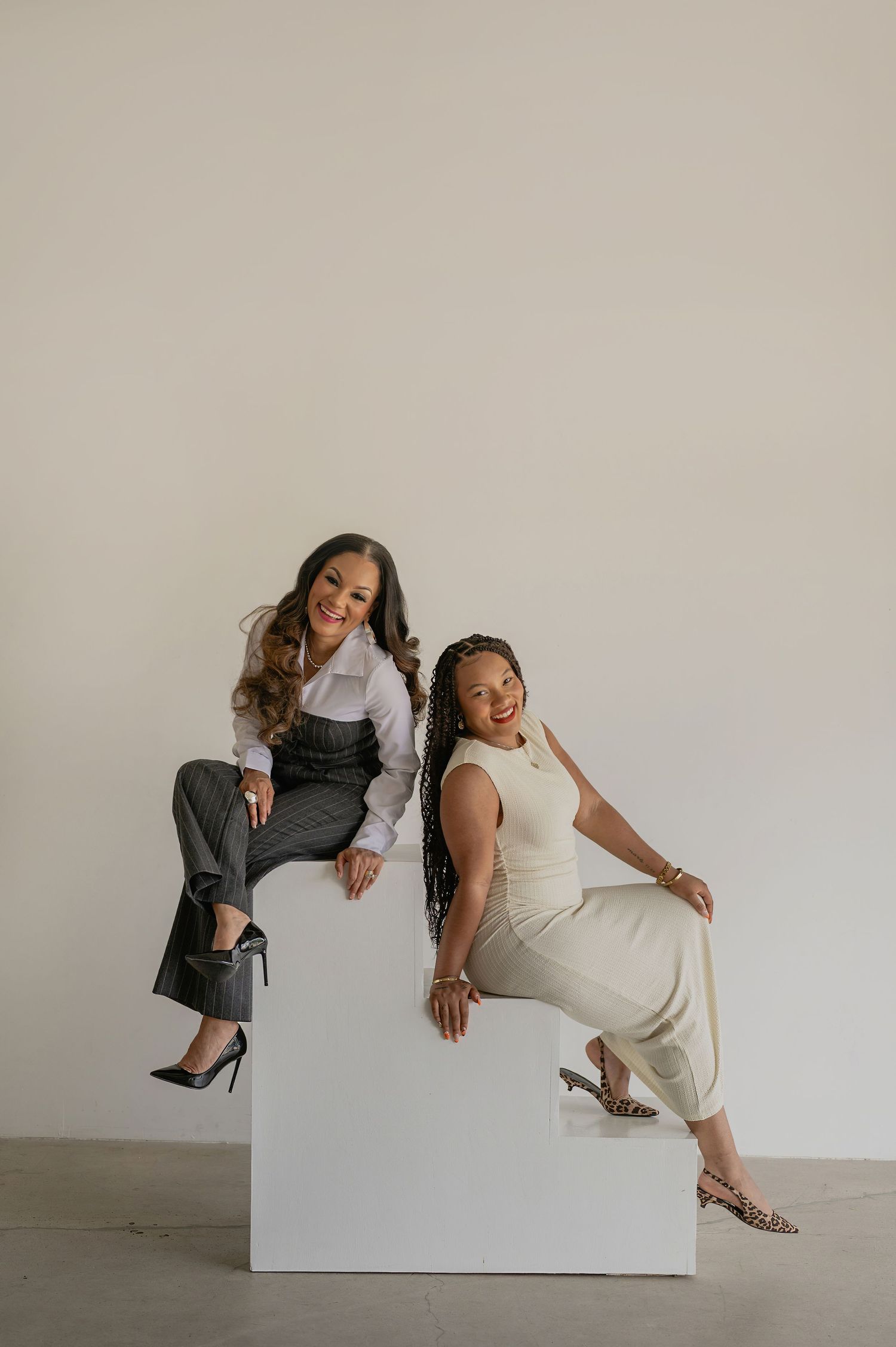 phoenix personal branding photos of two women posing on a white cube in a minimalist studio, one in gray trousers and one in cream jumpsuit.
