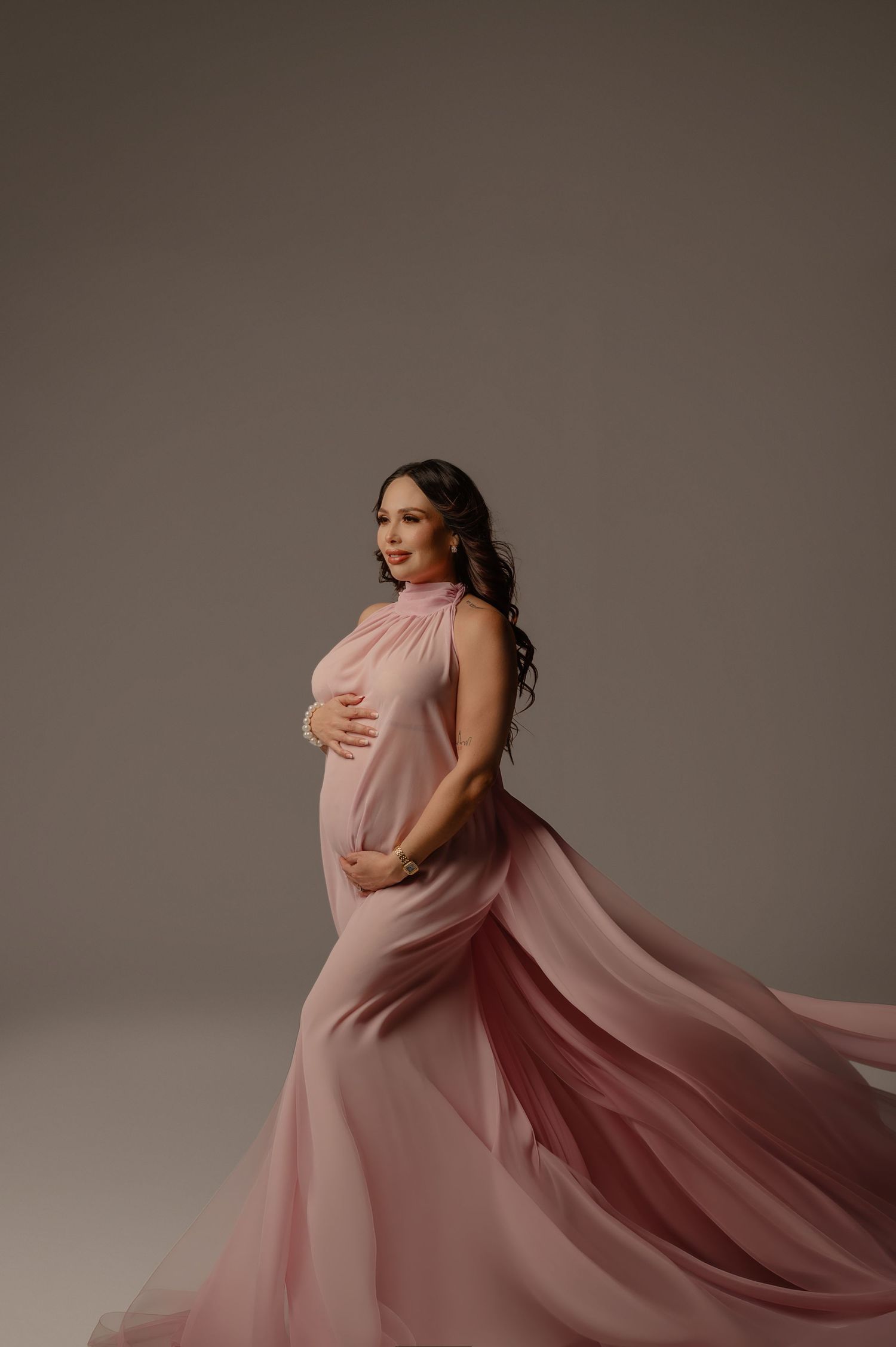 pregnant woman in a flowing pink gown poses against a studio backdrop in phoenix