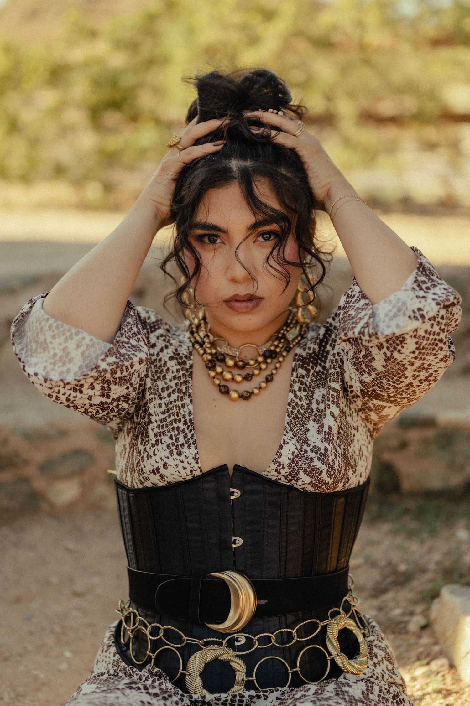 Fashion portrait of woman in metallic top and corset belt standing in the sun.