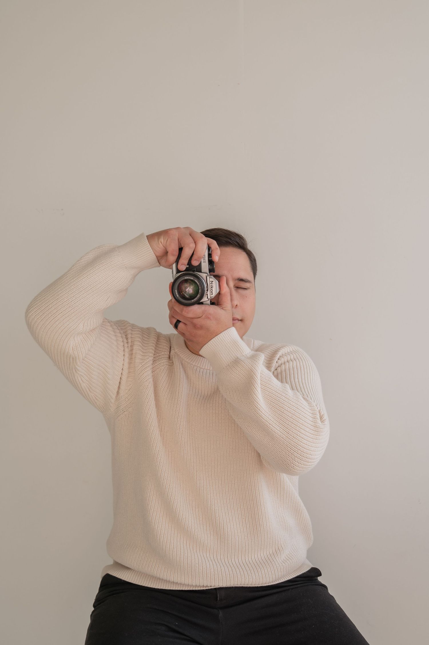 Man in white sweater holding up a film camera and smiling — lifestyle branding image capturing personality.