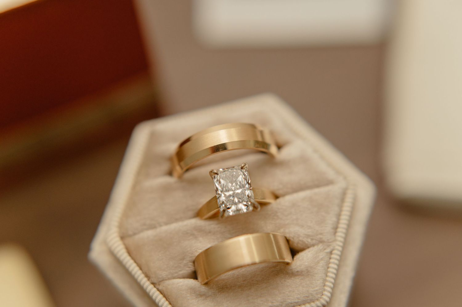 Close-up of engagement ring and two gold wedding bands in a velvet hexagon box.
