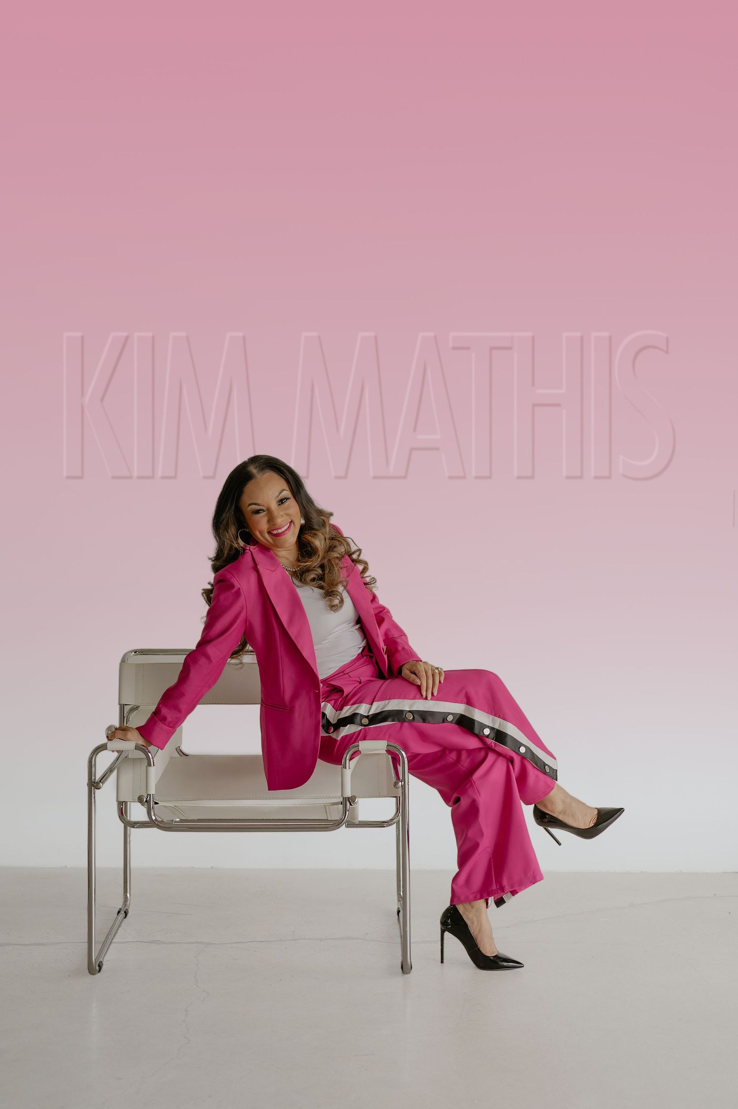 Woman in hot pink blazer and pants sitting confidently in chair on pink background.
