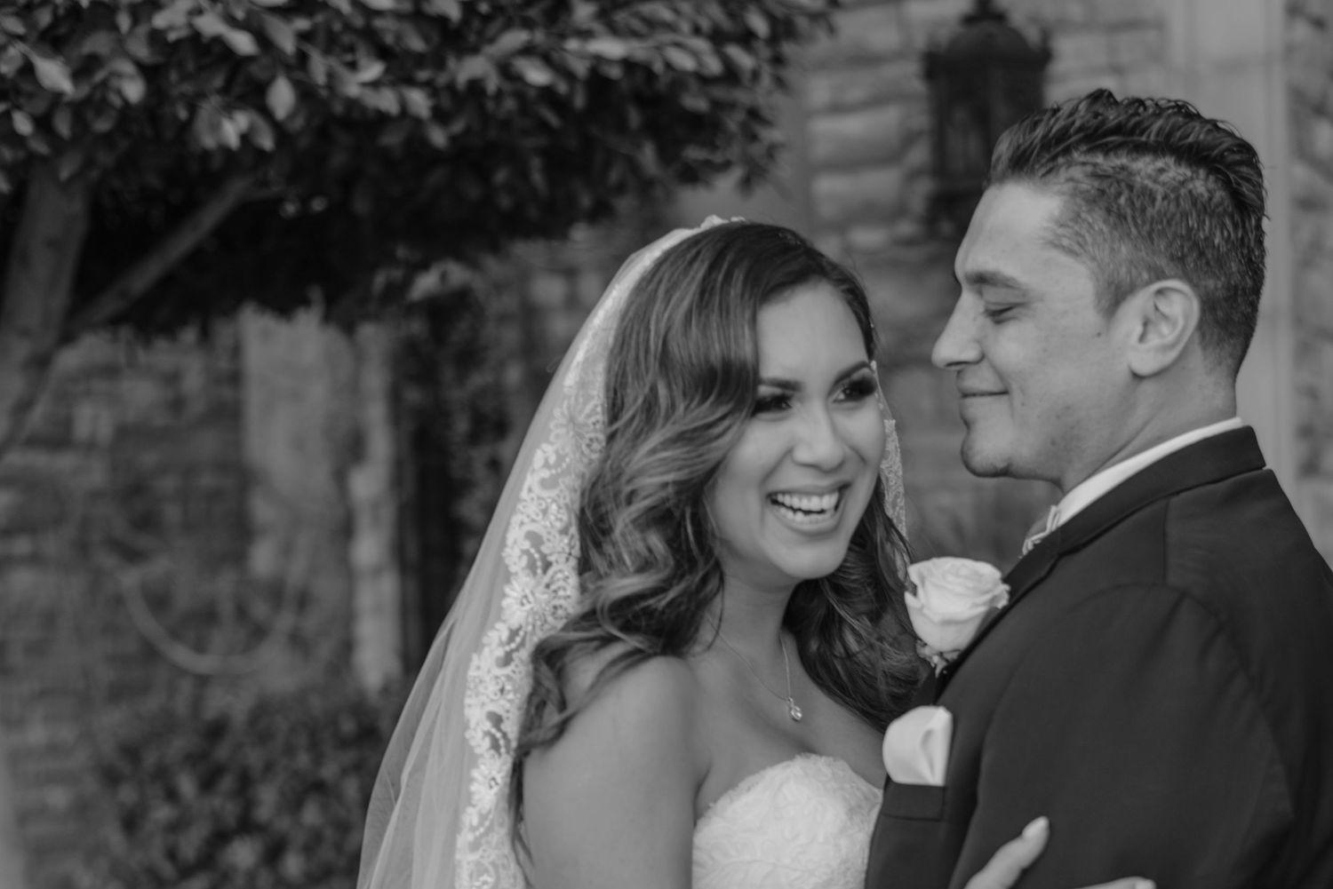 Black-and-white image of bride smiling at groom during candid moment.
