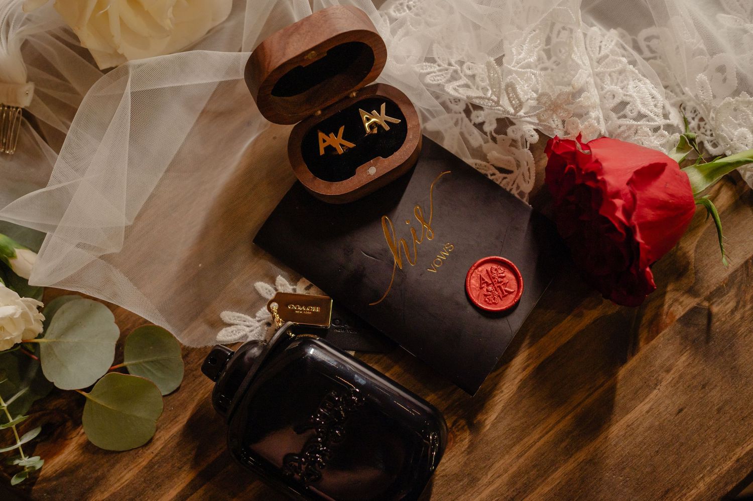 Groom’s wedding day flat lay featuring cologne, vow books, red rose, and accessories.