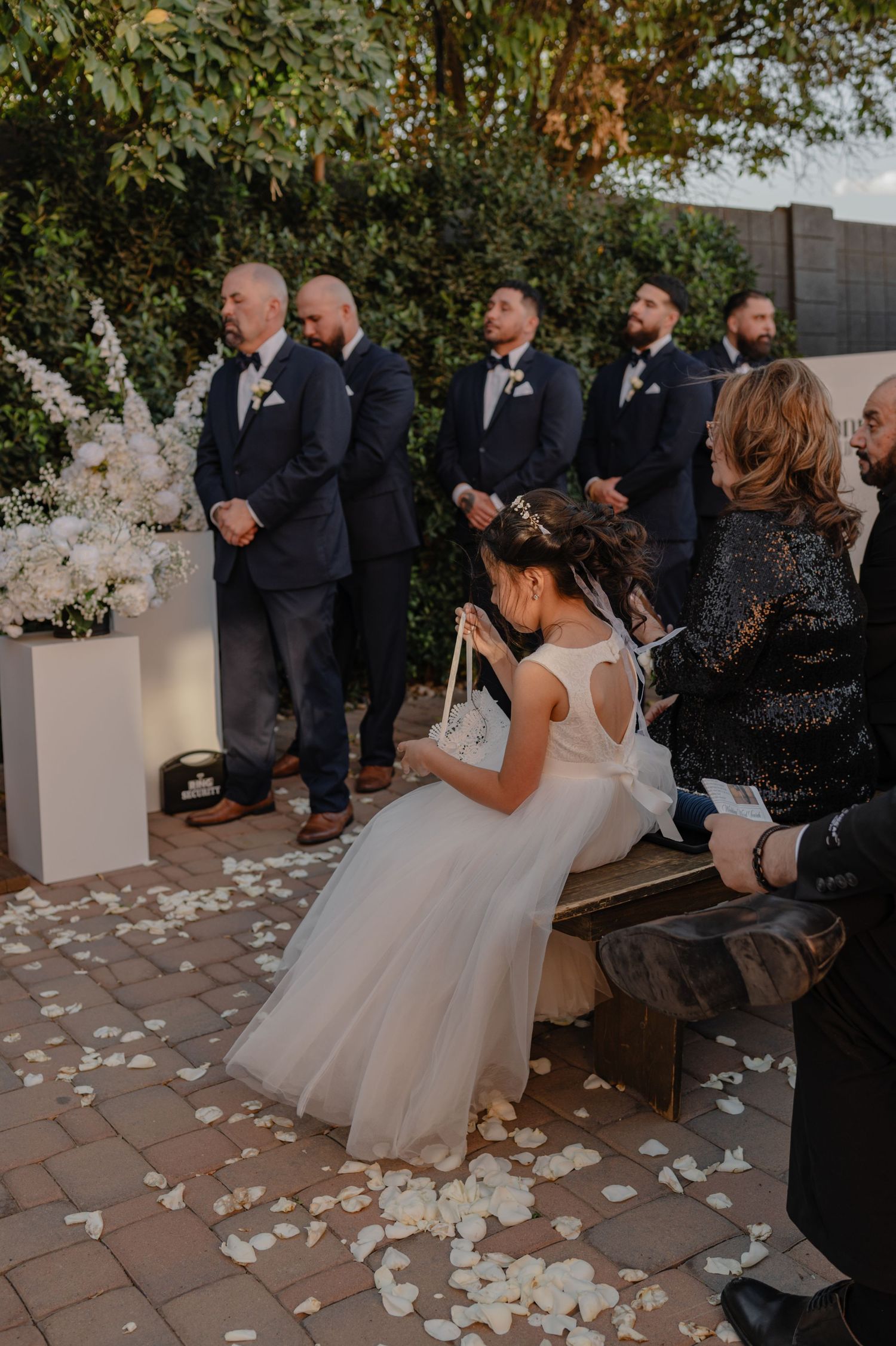 Bride sitting during outdoor ceremony, surrounded by guests and florals, under soft afternoon light.