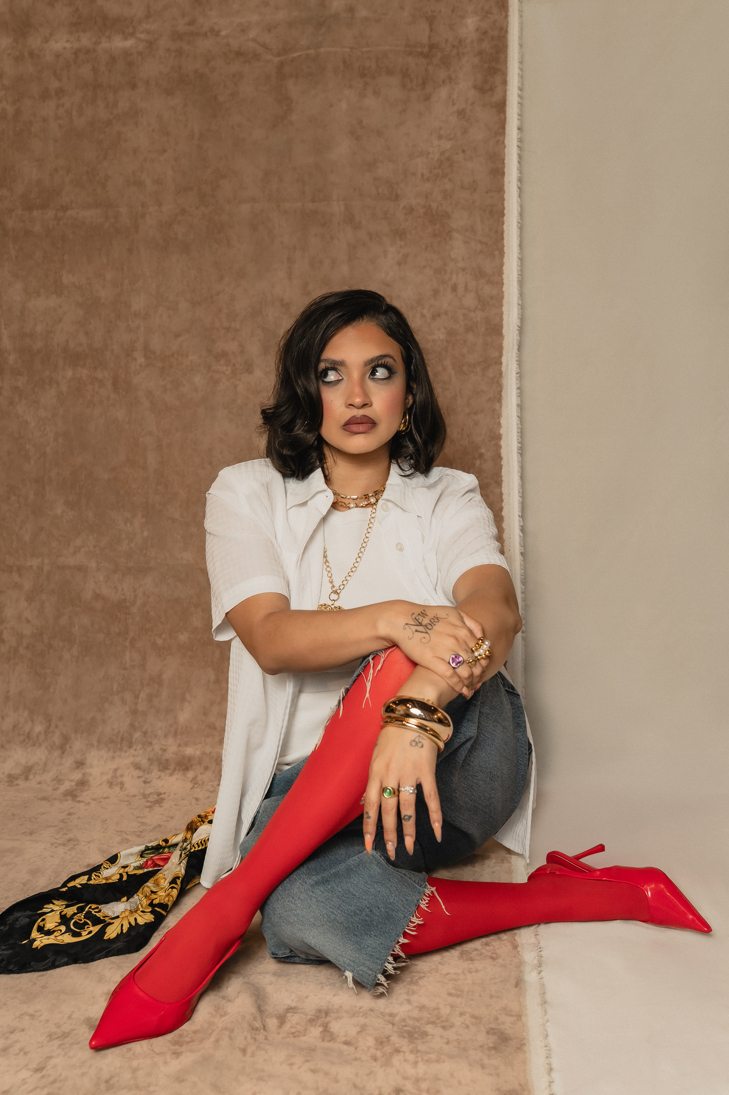 Bold studio brand portrait of woman seated in red heels and graphic tee, blending fashion and personality in a salon-inspired shoot.