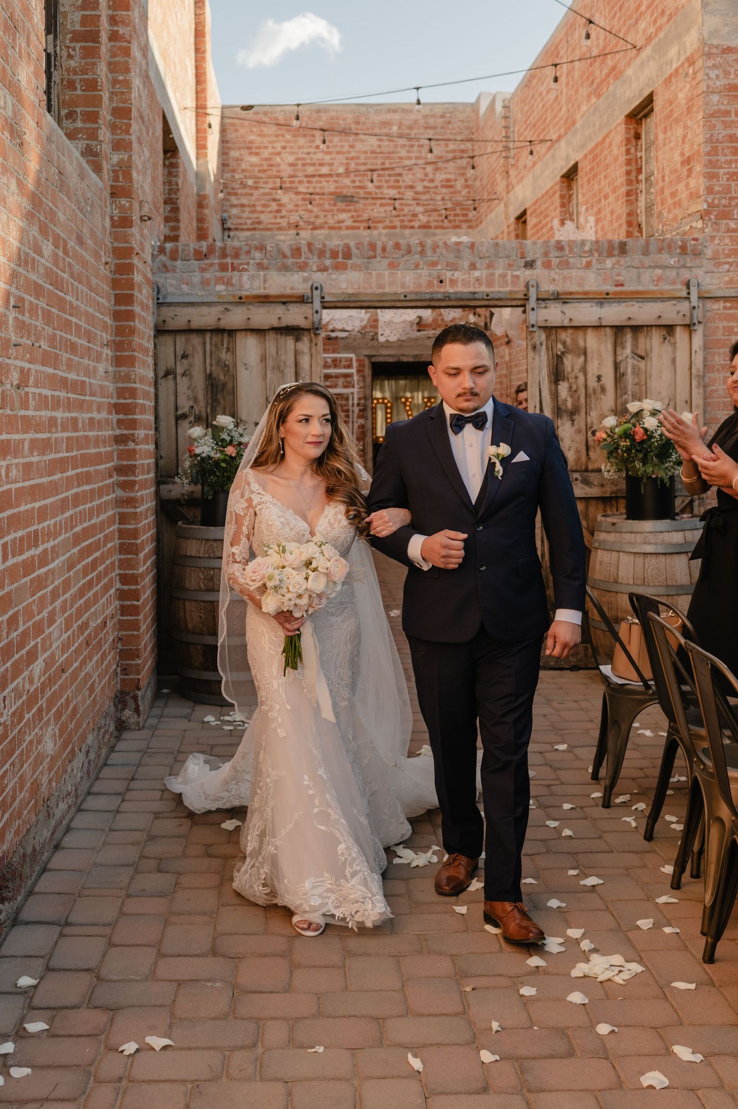 Bride and groom walk down narrow brick aisle between buildings after saying “I do,” glowing with post-ceremony joy.
