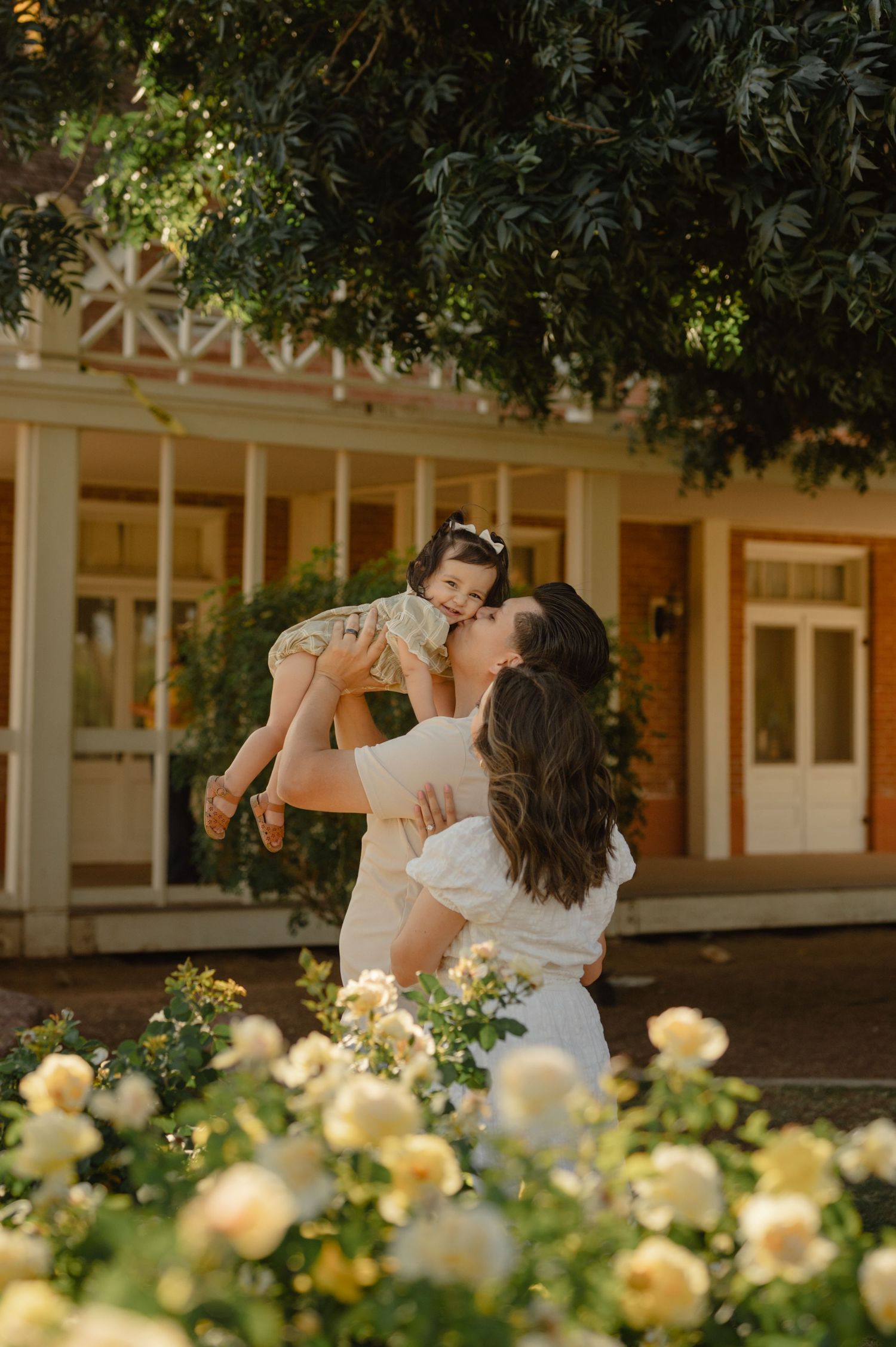 A mother lifts and kisses her toddler among yellow roses at Sahuaro Ranch Park in Glendale, AZ.