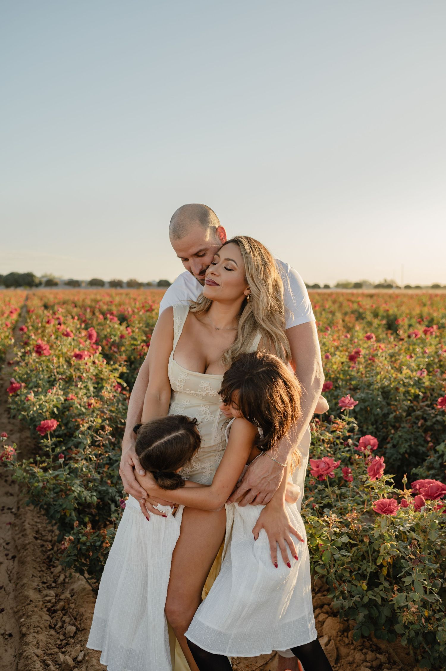 Rosy Liddi, founder of Calma Wellness Lounge, embraces her family in a blooming rose field at golden hour.