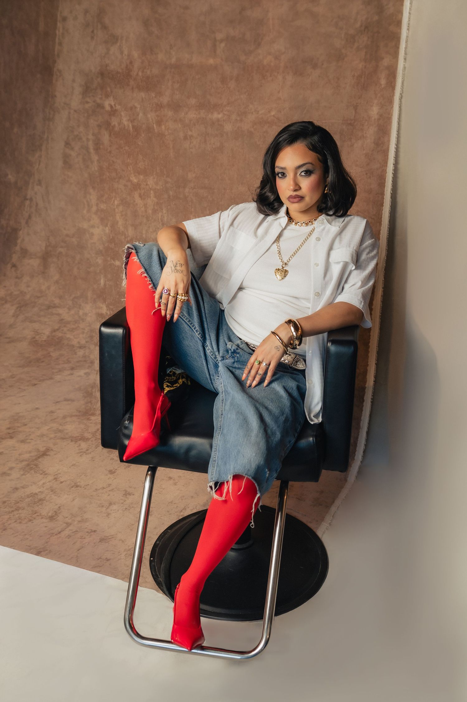 Confident woman with red heels reclines in a black chair, hands on hips — a bold pose from The Hive Salon shoot.