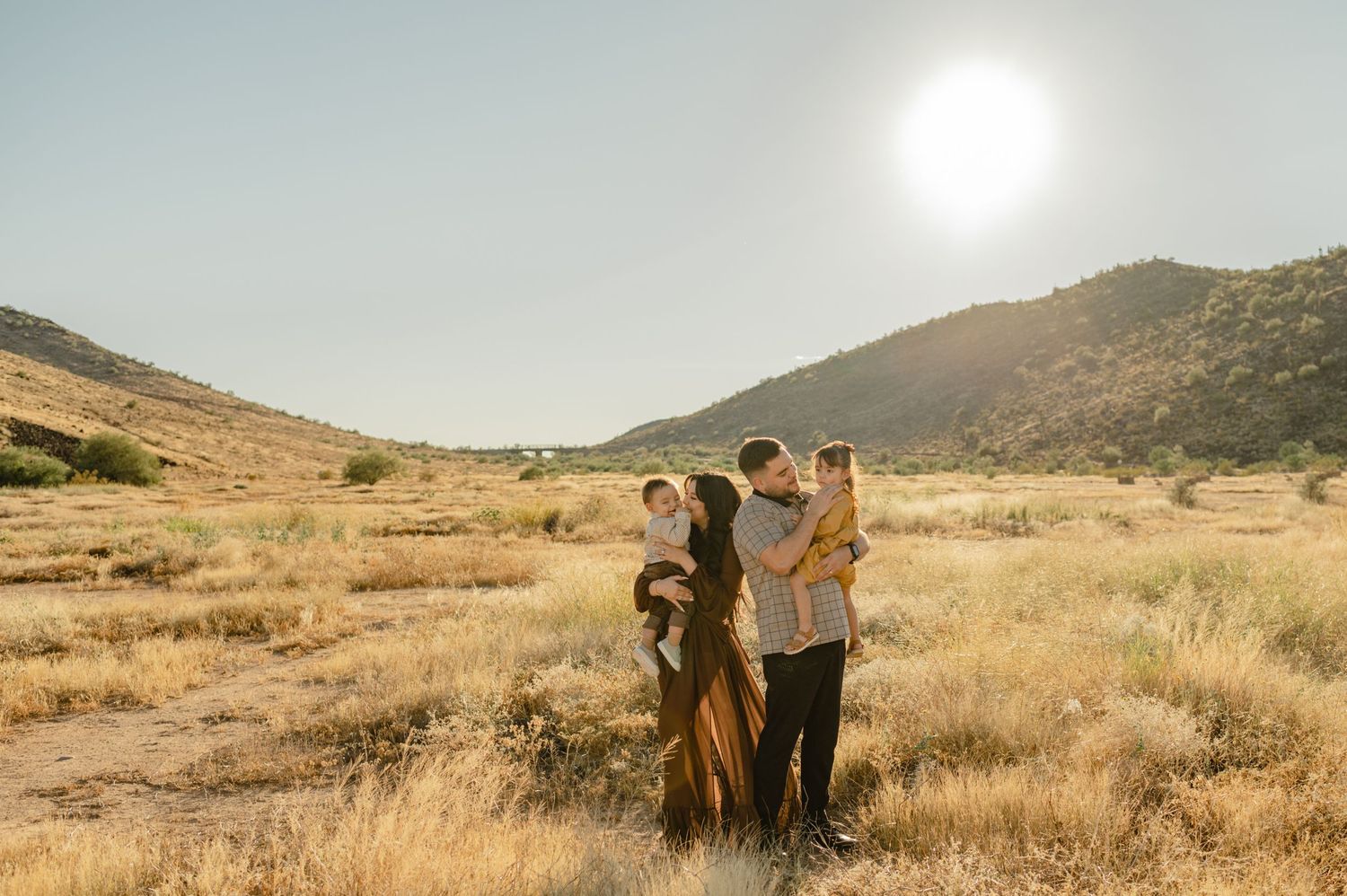 family with two young children embraces in golden hour light at thunderbird conservation park in glendale, arizona