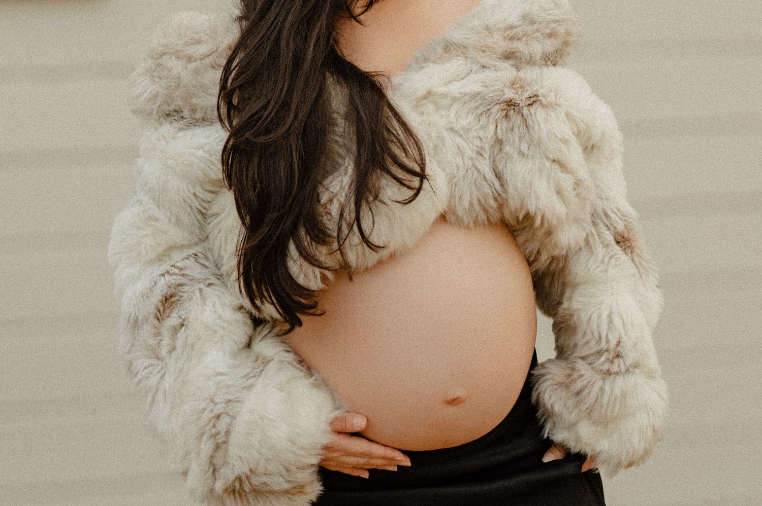 pregnant woman in a faux fur coat cradles her bump during a phoenix studio maternity session