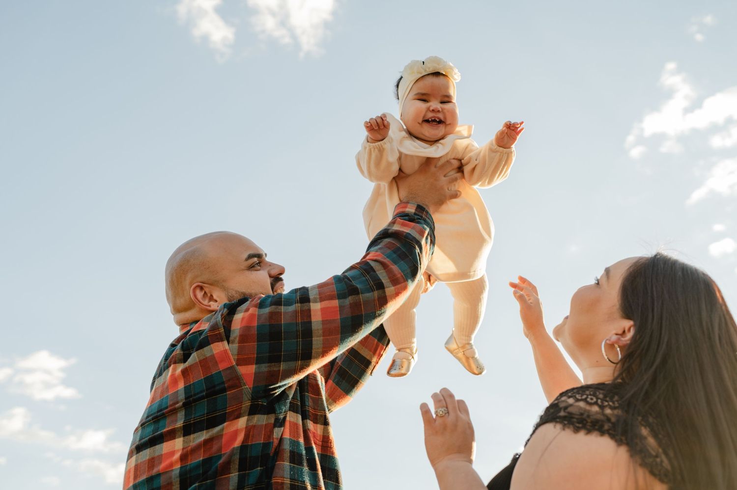 Parents lift their smiling baby high against a bright blue sky during a family session in Payson, AZ.