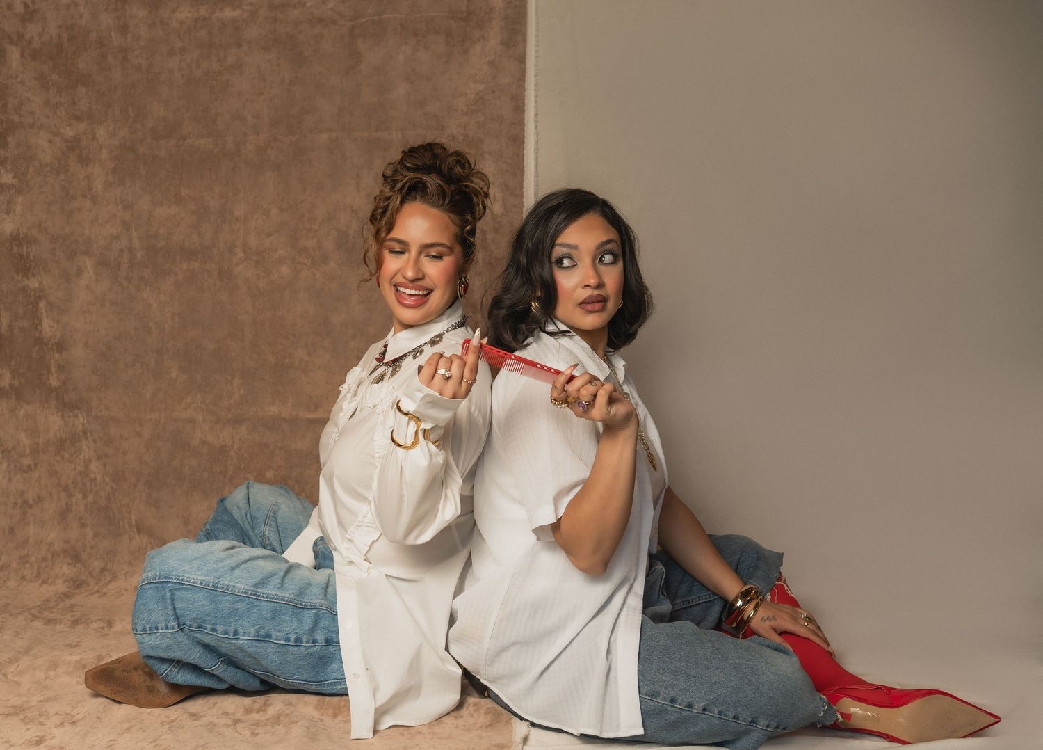 Two women pose on the floor with curling irons and playful expressions — a fun moment from The Hive Salon shoot.