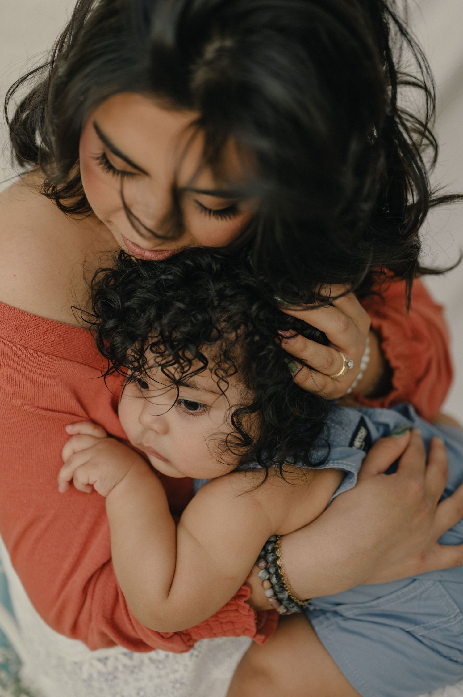 Amariz Jones tenderly embraces her curly haired baby outdoors, a warm family portrait moment.