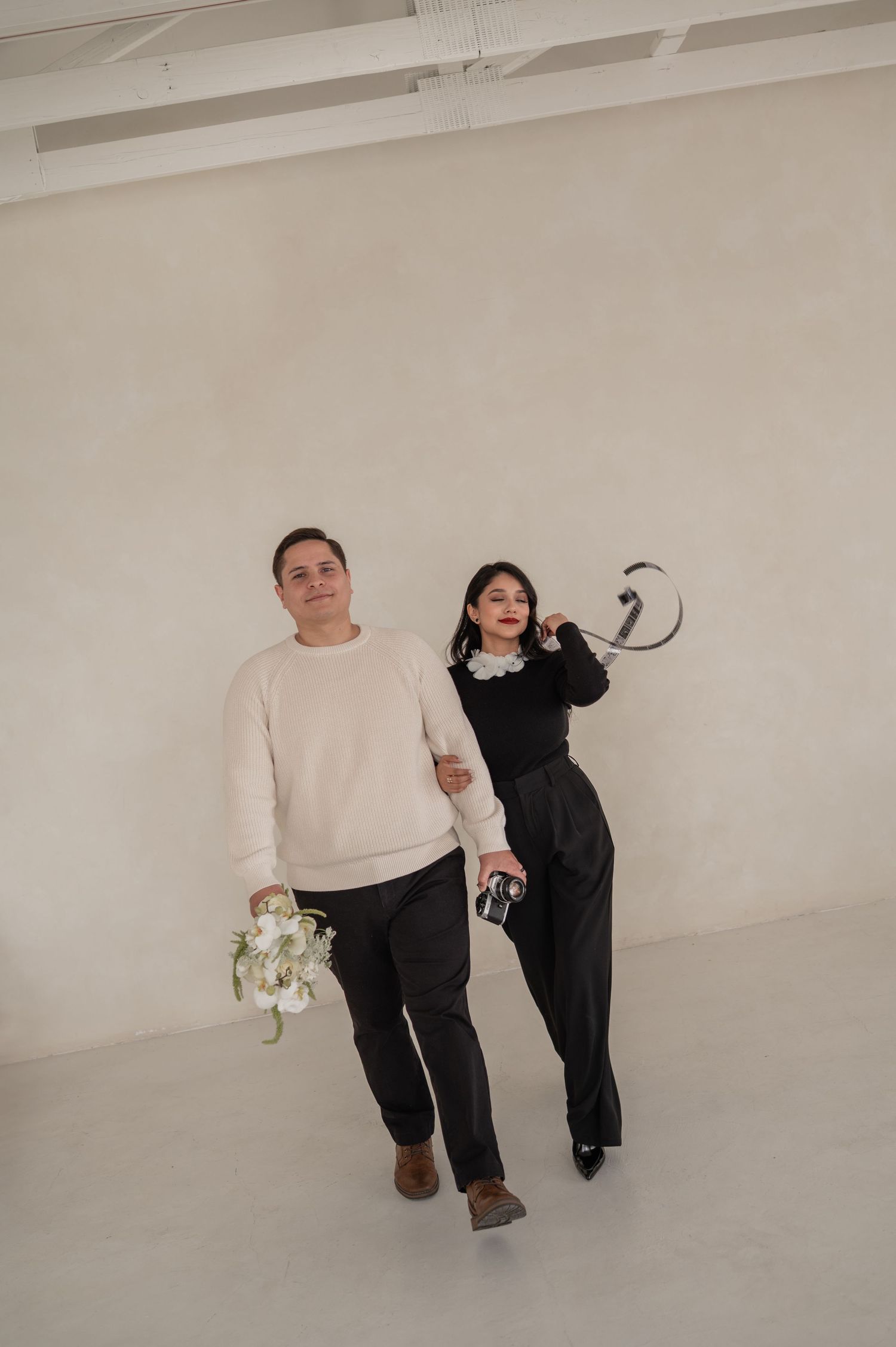 Two photographers posing together in studio attire, holding camera and florals — team portrait introducing brand founders.