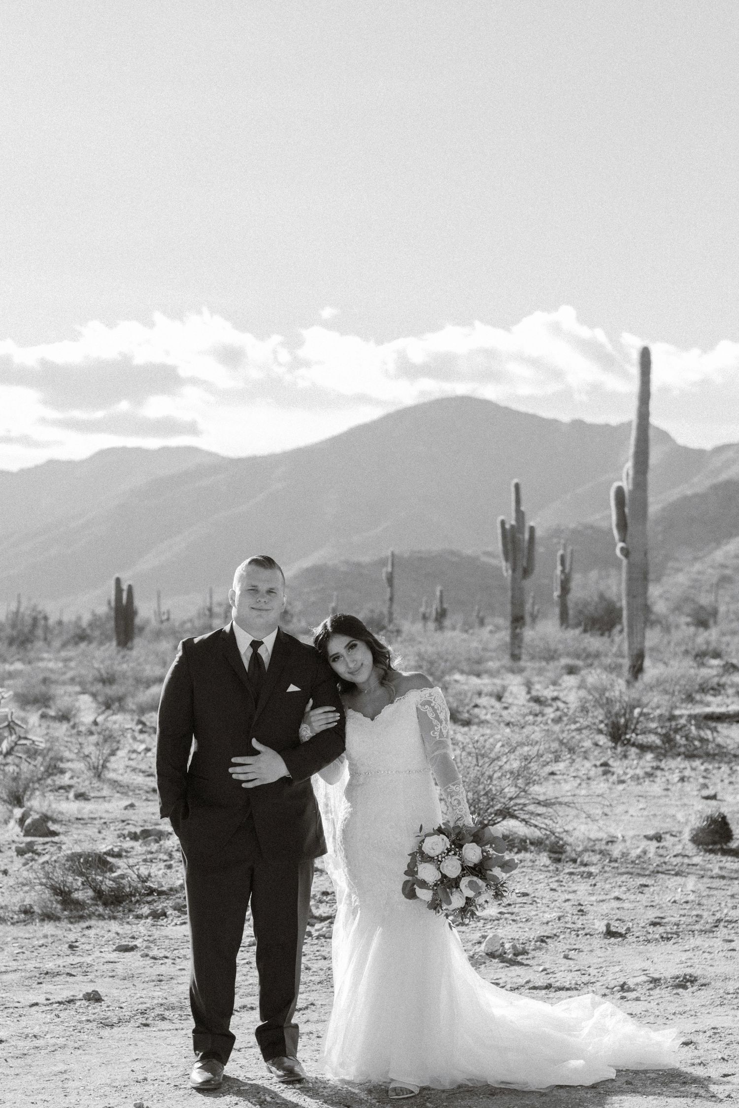 Black-and-white portrait of couple holding hands in desert landscape with cacti.