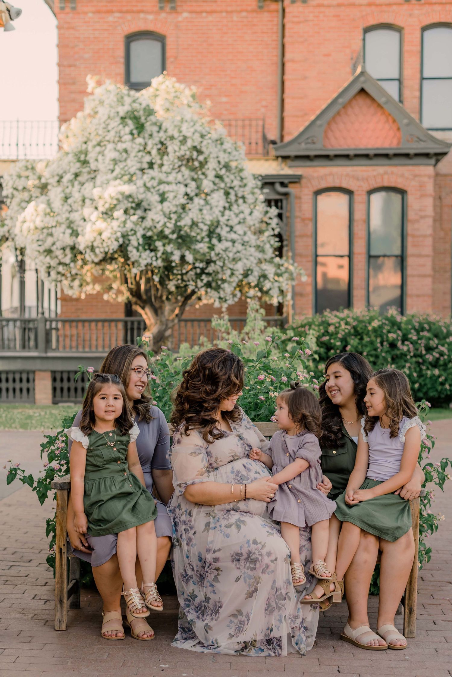 pregnant mom poses with her daughters on a garden bench during a phoenix maternity photography session at heritage square