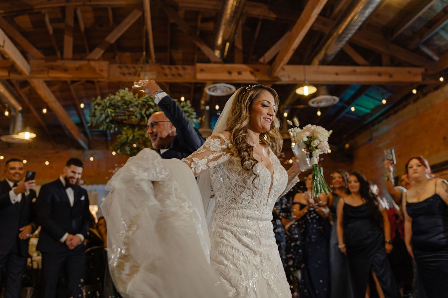 Bride and groom walking down the aisle, cheering, with guests and florals inside a modern rustic wedding venue.