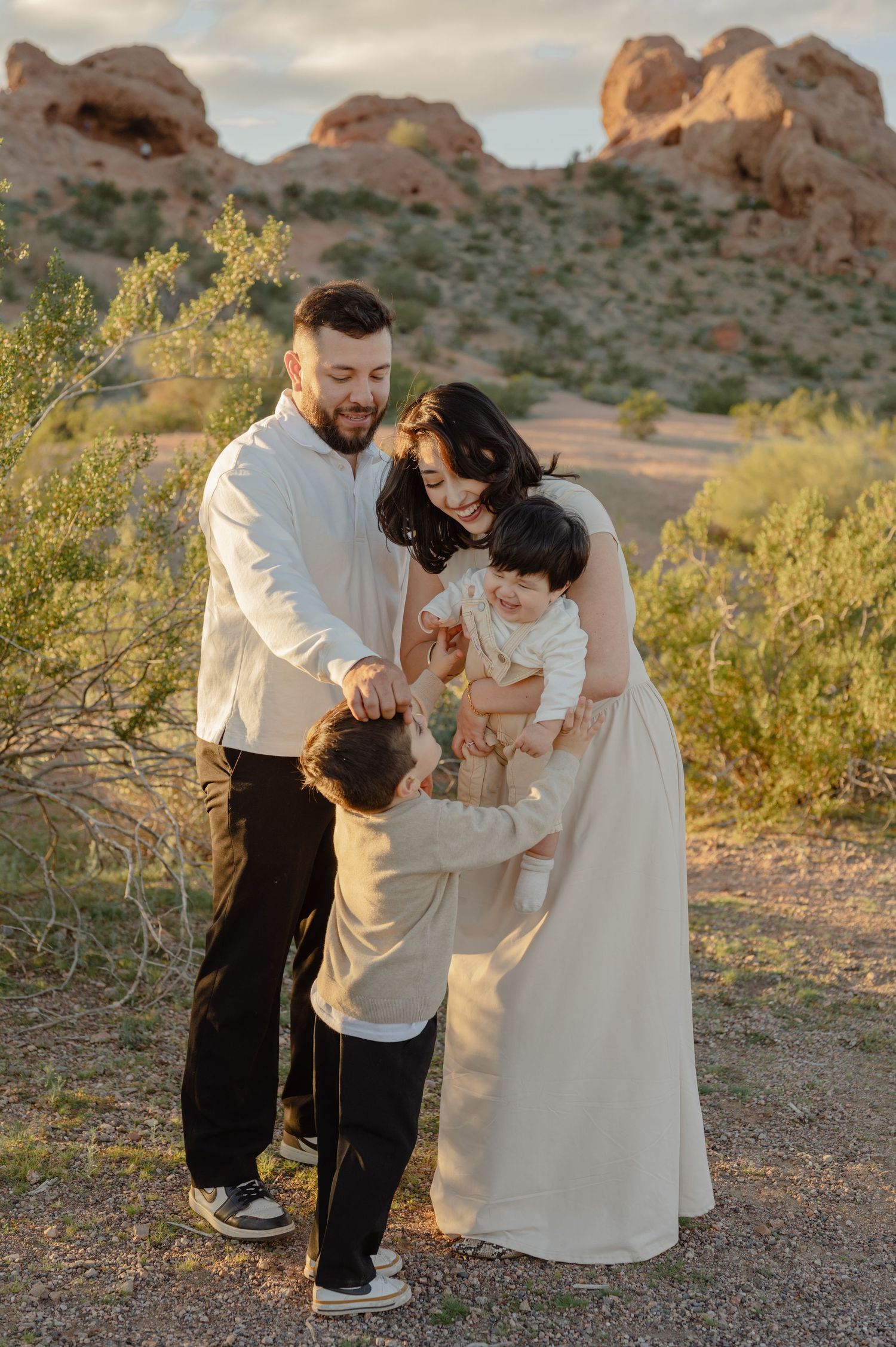 A family of four plays together at golden hour among the red rock formations of Papago Park, a family photography session in Phoenix, AZ.
