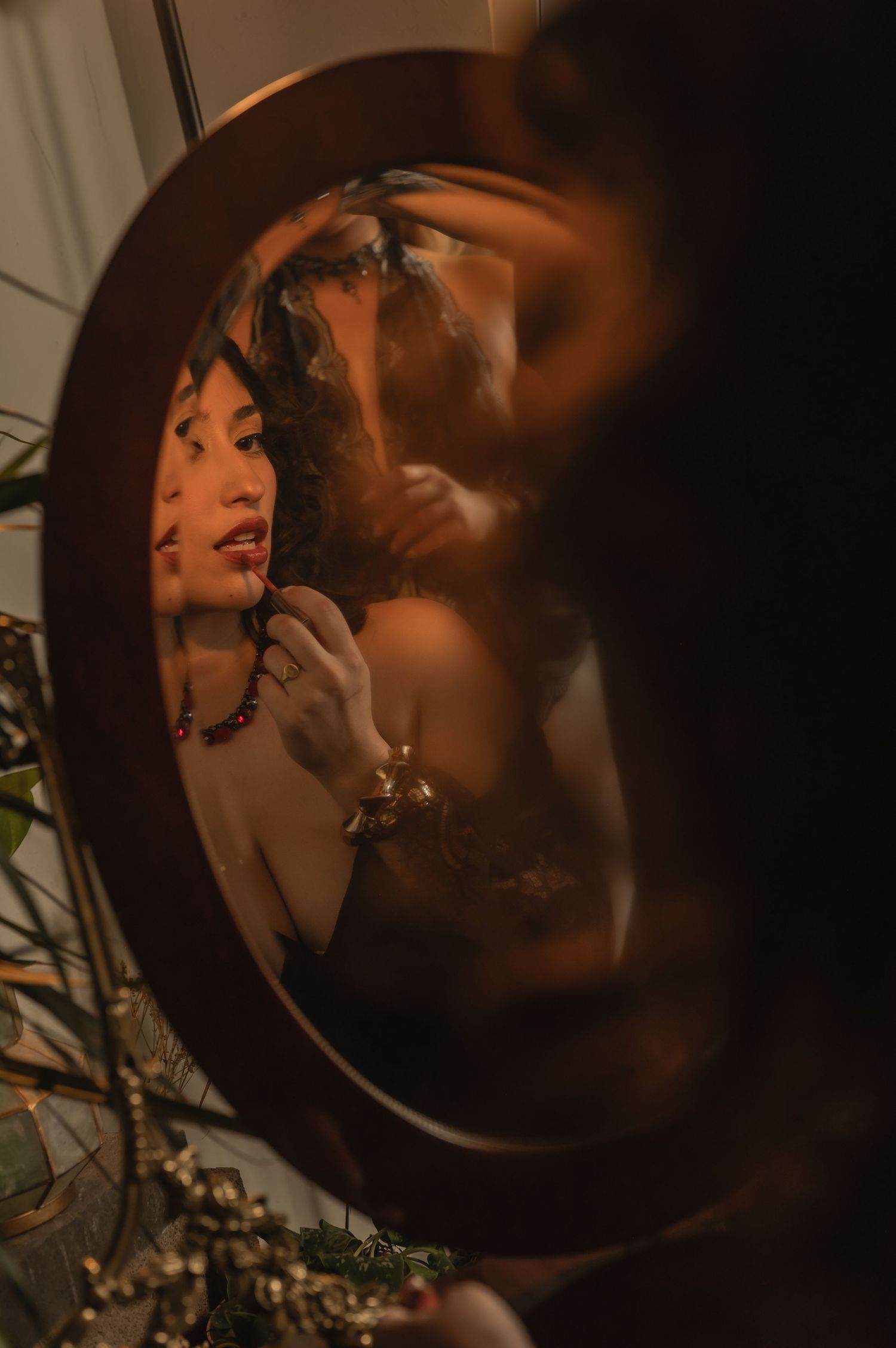 Moody double reflection in salon mirror showing a woman preparing with beauty tools and florals.