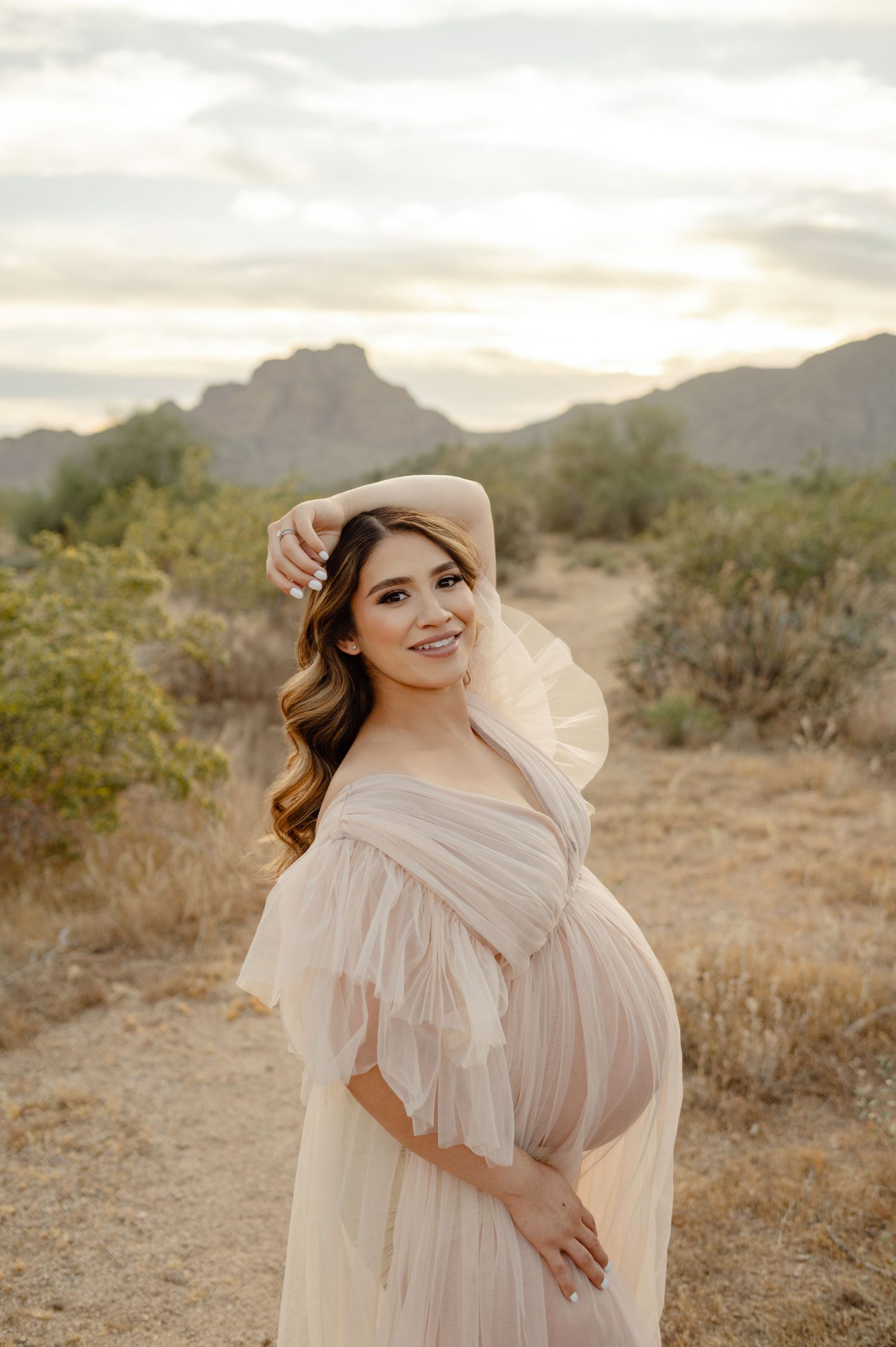 pregnant woman poses in a flowing gown among desert mountains at golden hour in phoenix