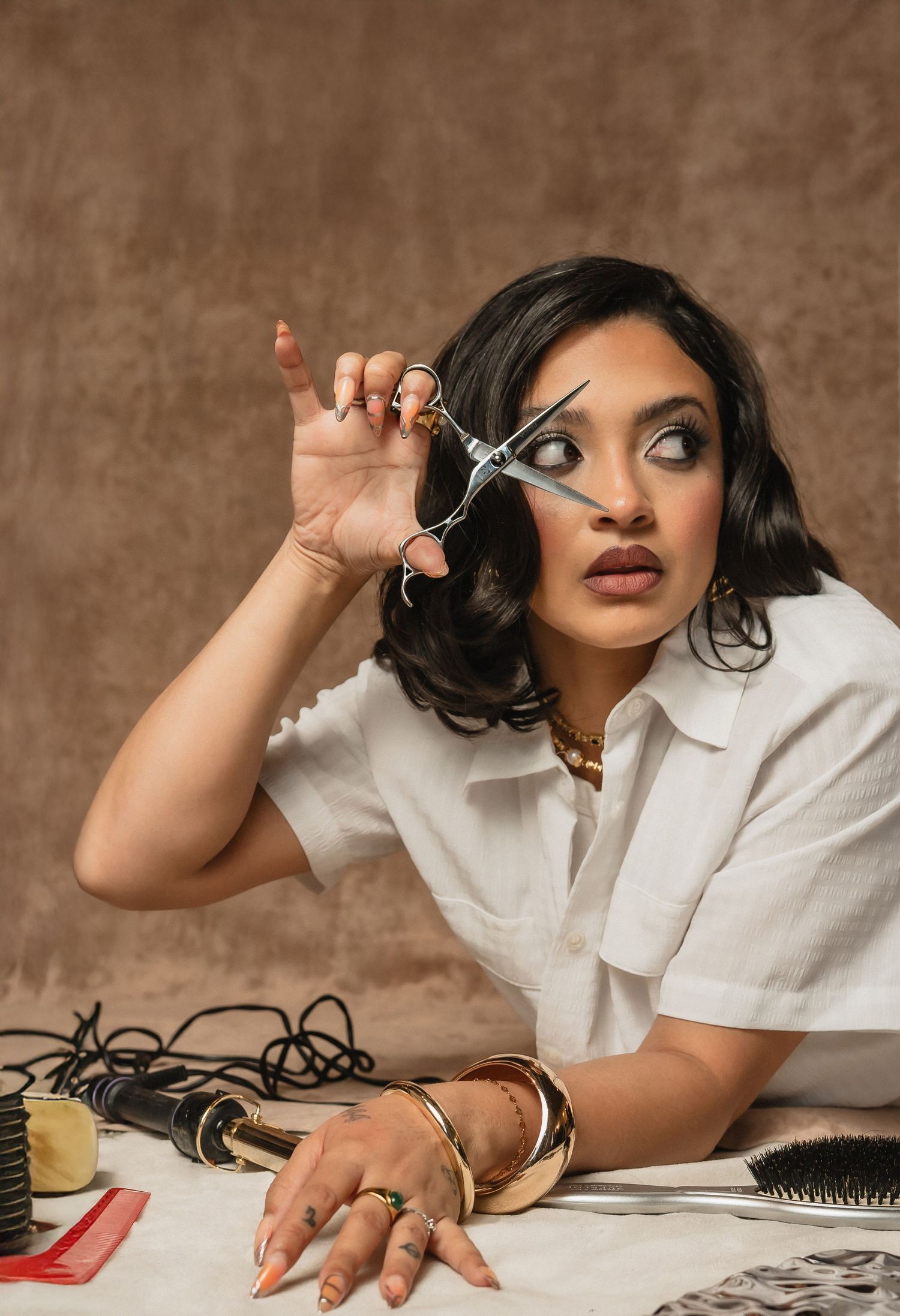 Woman in a white blouse looking off to the side while holding scissors — styled at The Hive Salon.