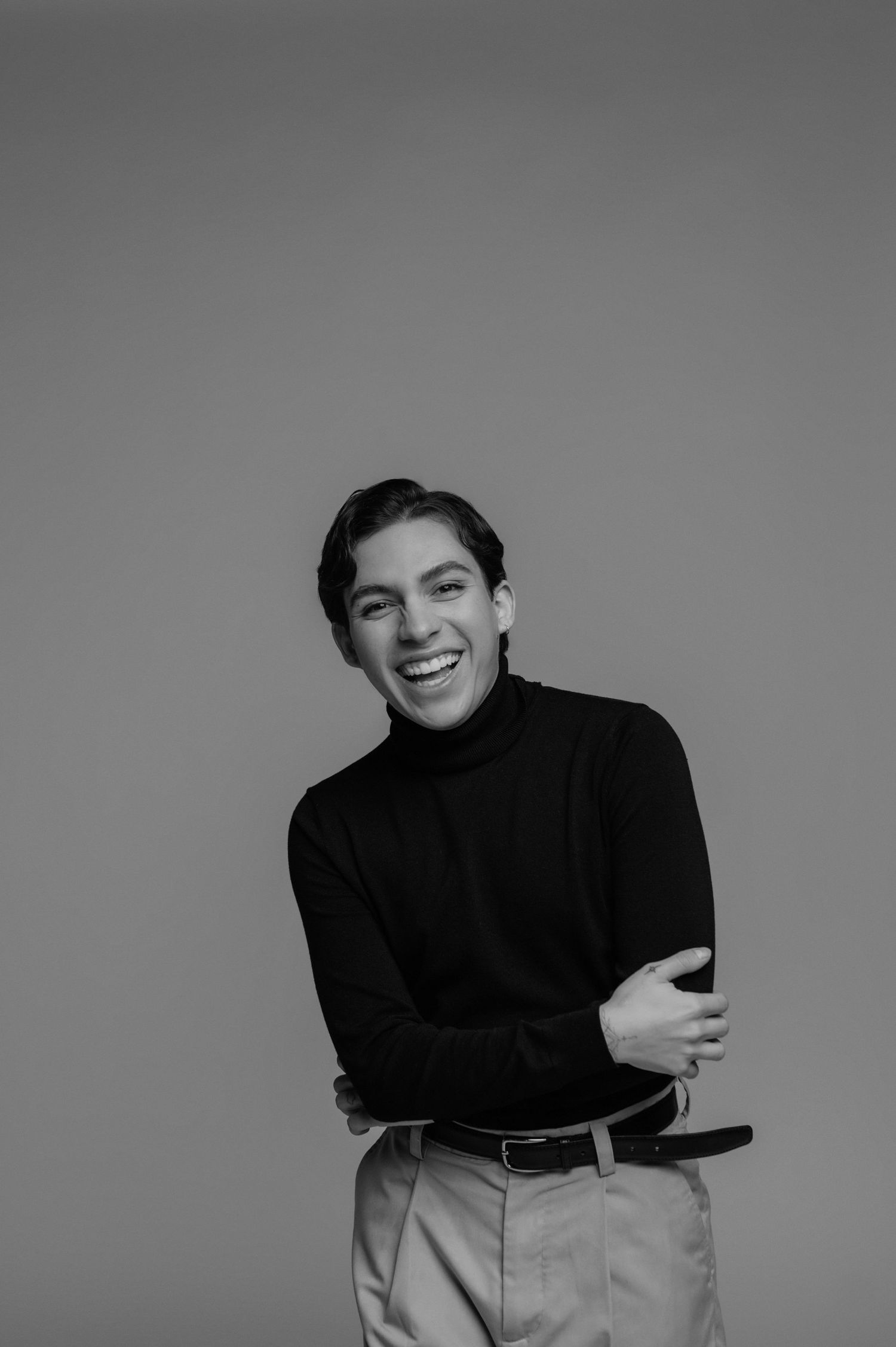 Young man in black turtleneck smiling confidently, arms crossed, black and white studio portrait photo in phoenix arizona.