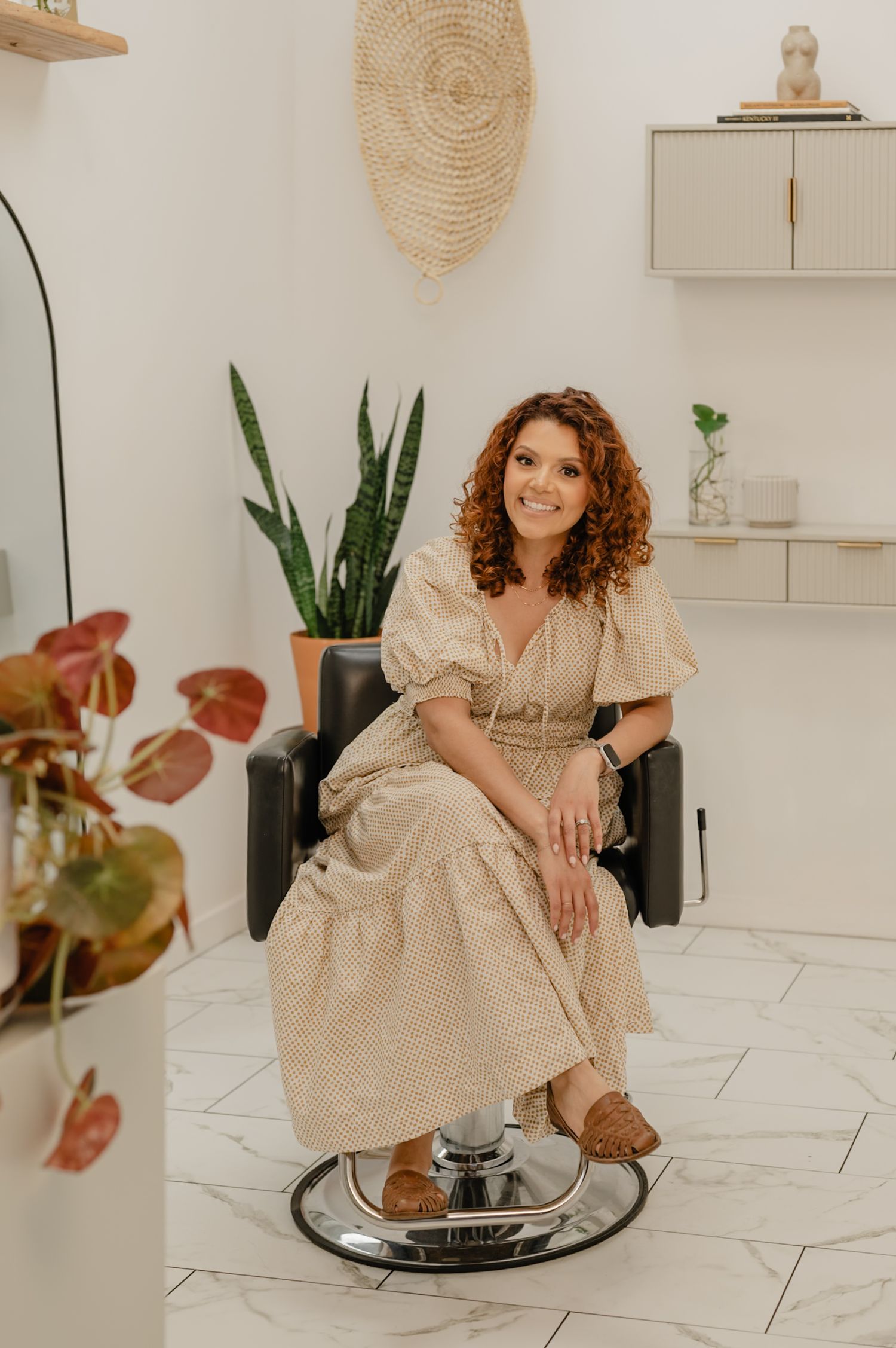 Serena seated in her salon chair with plants and textures around her during a warm, lifestyle brand shoot.