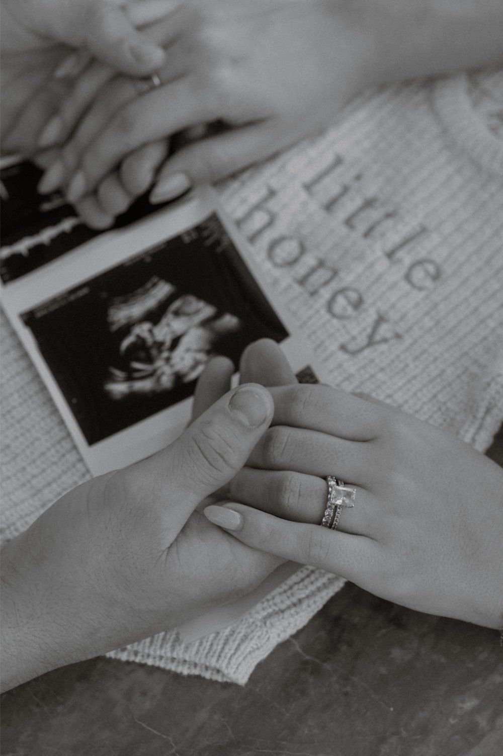 Black and white close up of hands holding a sonogram photo reading little honey