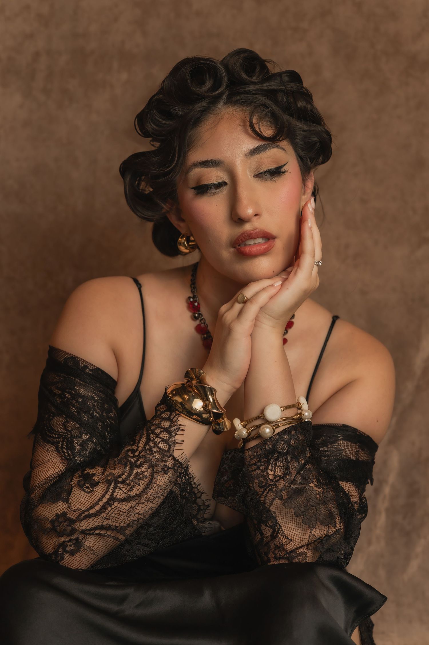 Woman with vintage pin curls and lace gloves poses against a warm-toned backdrop — part of The Hive Salon shoot.