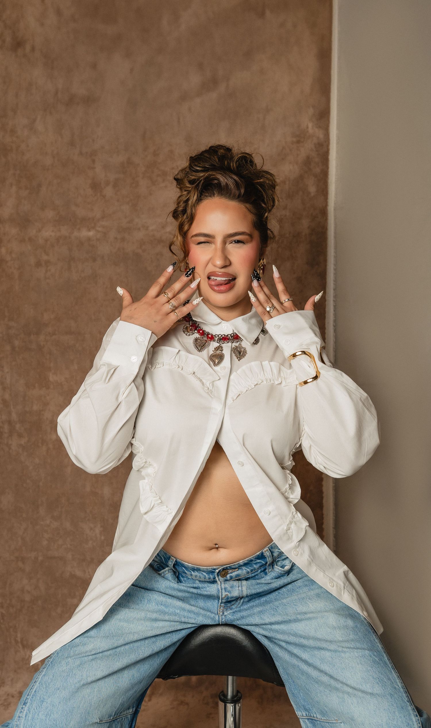 Woman poses playfully with curling iron in one hand and teasing brush in the other.