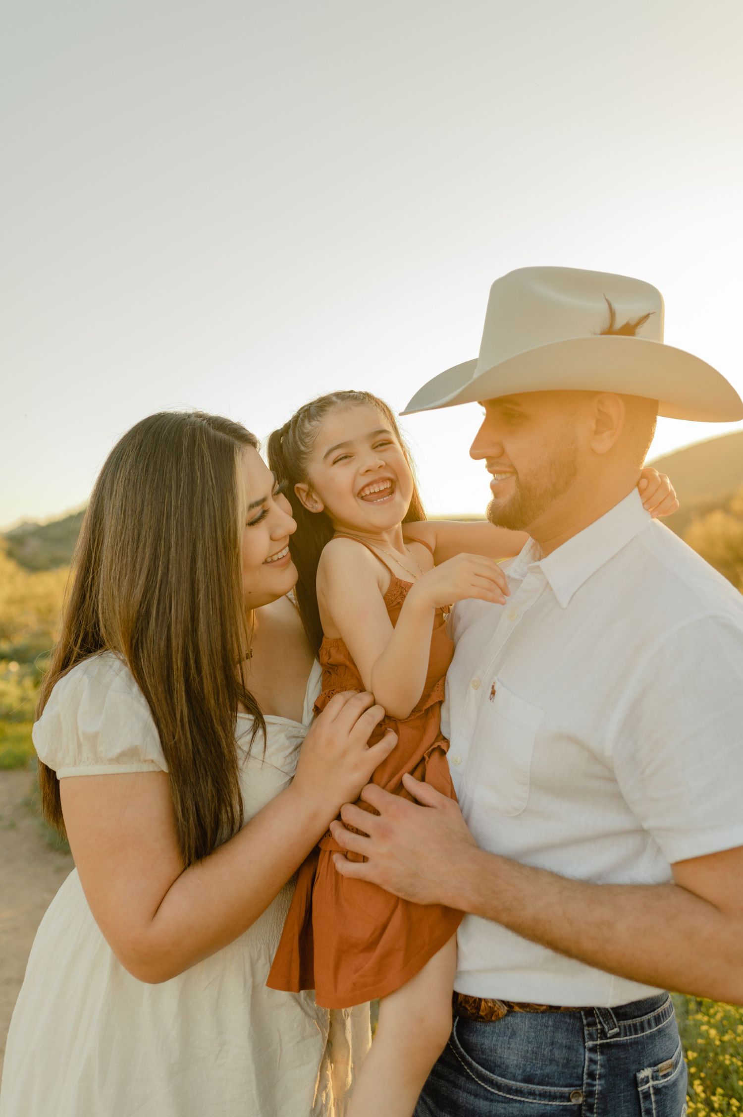 Gabriela's family laughs together in golden light at Jewel of the Creek, dad in a cowboy hat lifting his daughter.