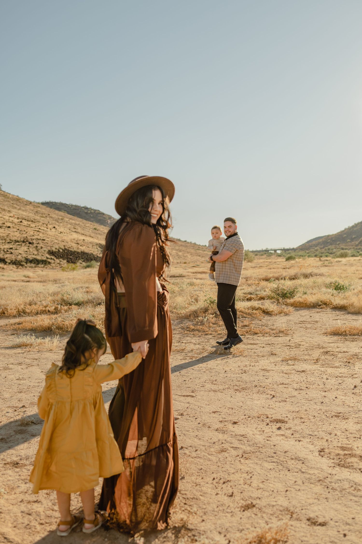 A mother holds her daughter's hand while her partner carries their baby across the desert at Thunderbird Conservation Park, AZ.