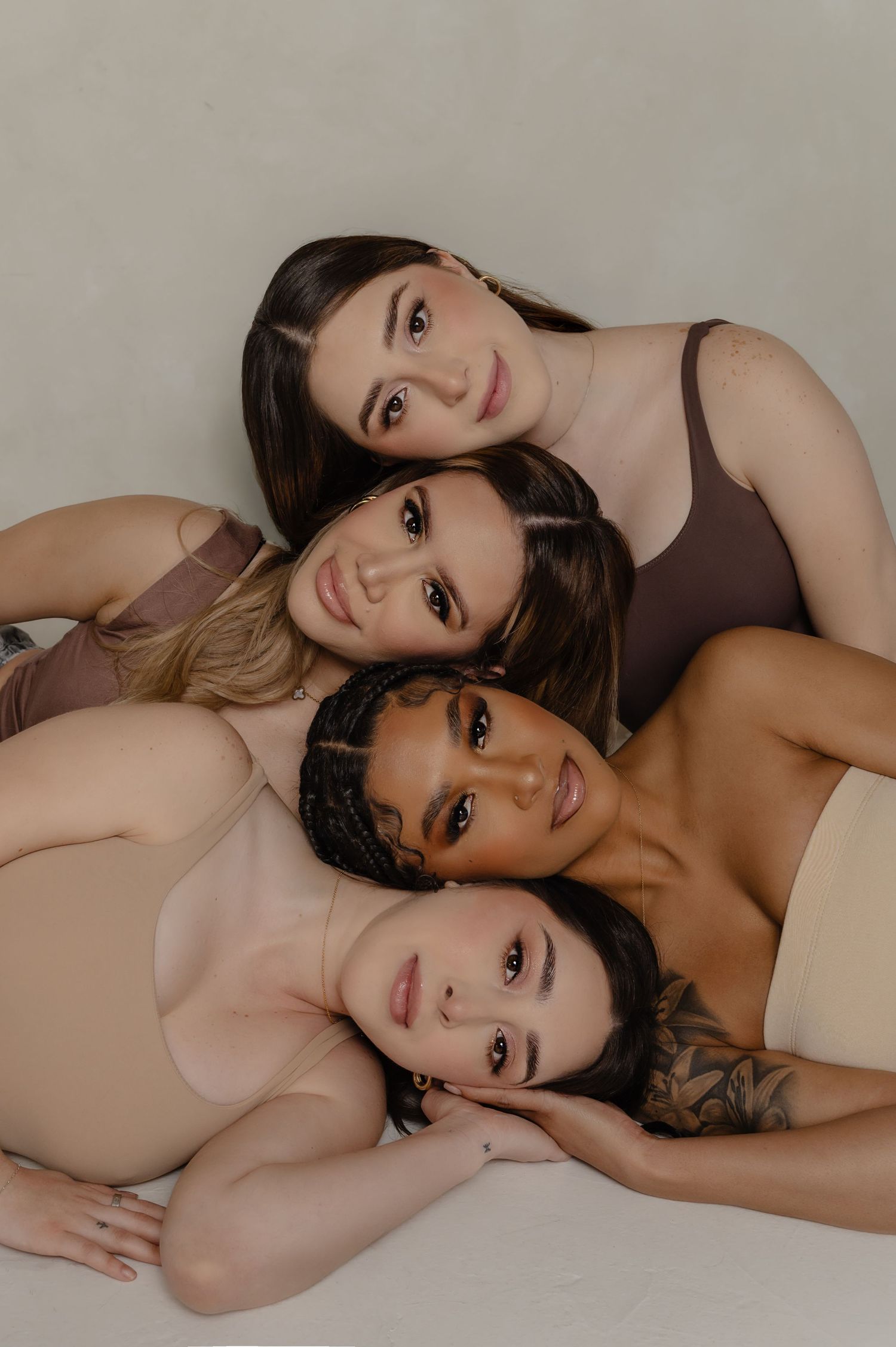 Four diverse women in neutral-toned bodysuits posing together against a light background.