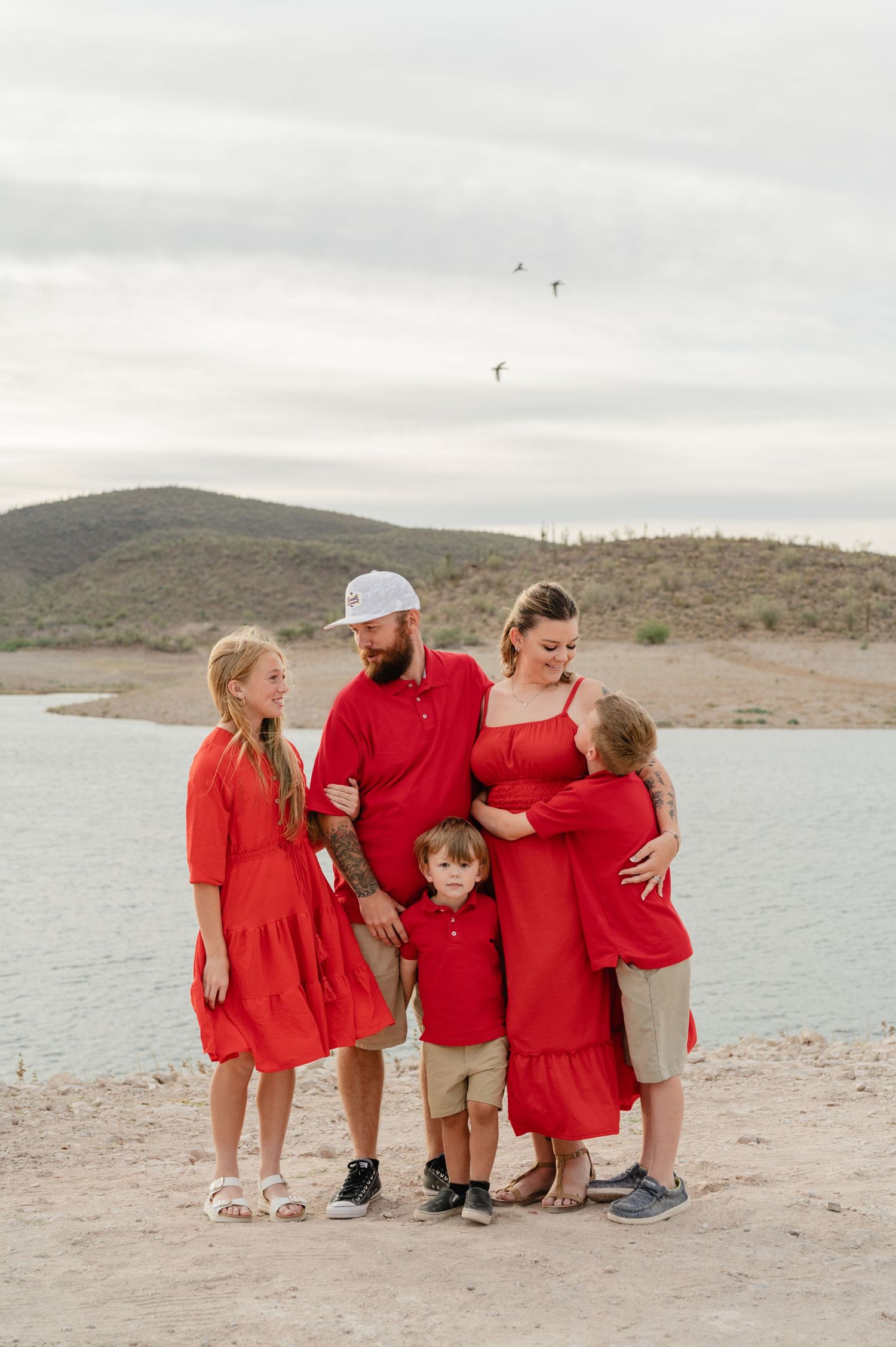 Family of five in red outfits posing together near a scenic lake and hills.