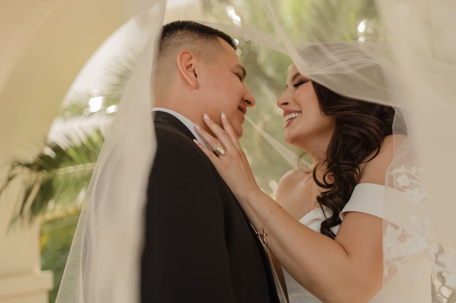 Bride and groom smiling under veil during first look, captured with warm golden light and romantic energy.
