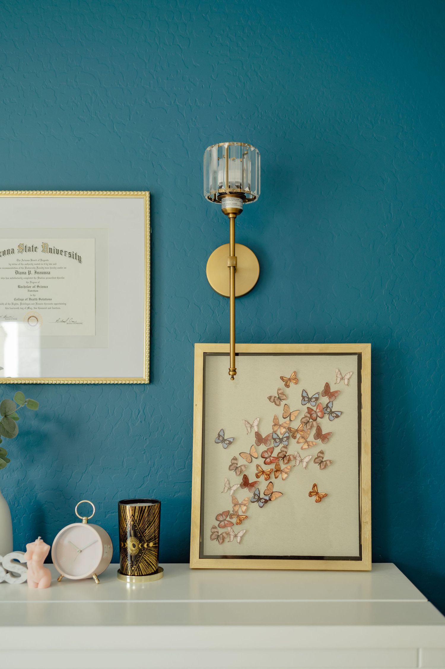 Minimal styled shot of the teal wall with art prints and stacked books — curated brand environment.