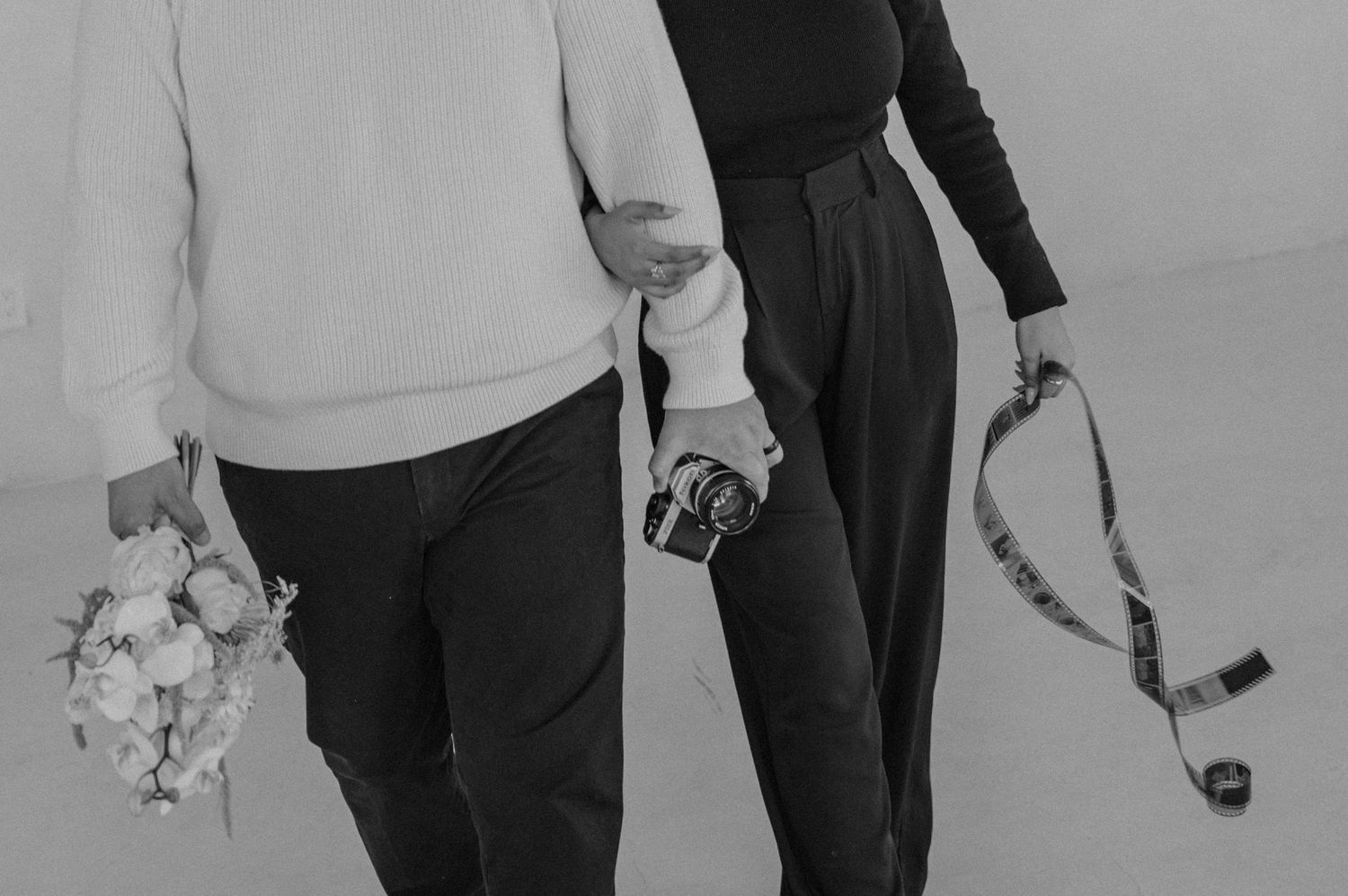 Detail of a couple holding hands and a bouquet of flowers — black-and-white editorial styling.