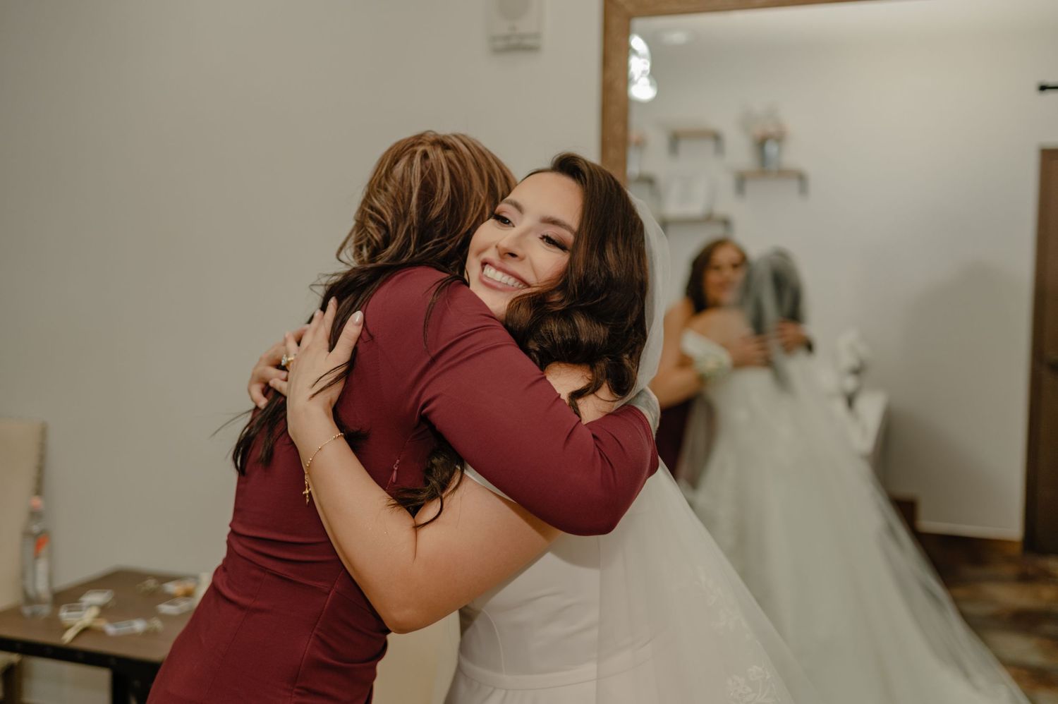 Bride shares joyful hug with guest in the bridal suite, bridesmaids visible in the background.