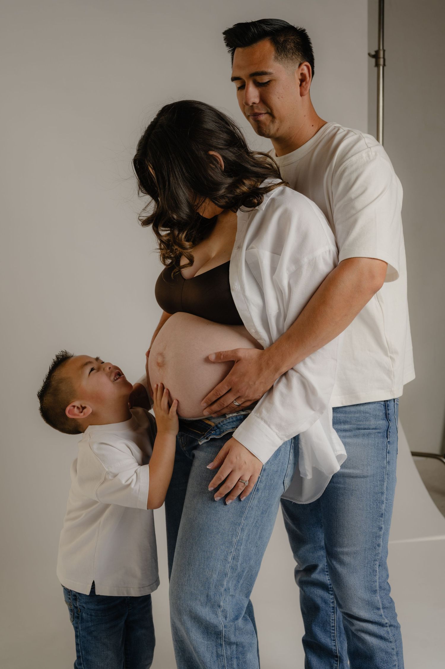 young son looks up at his pregnant mom while dad holds her bump during a phoenix studio maternity session