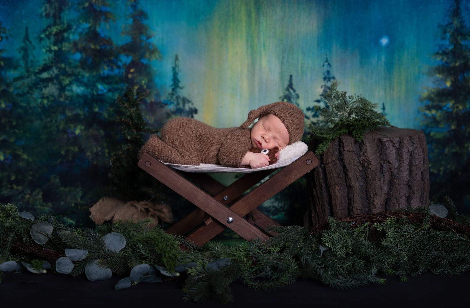 A peaceful newborn sleeps in a rustic wooden bed surrounded by a dreamy forest-themed backdrop.