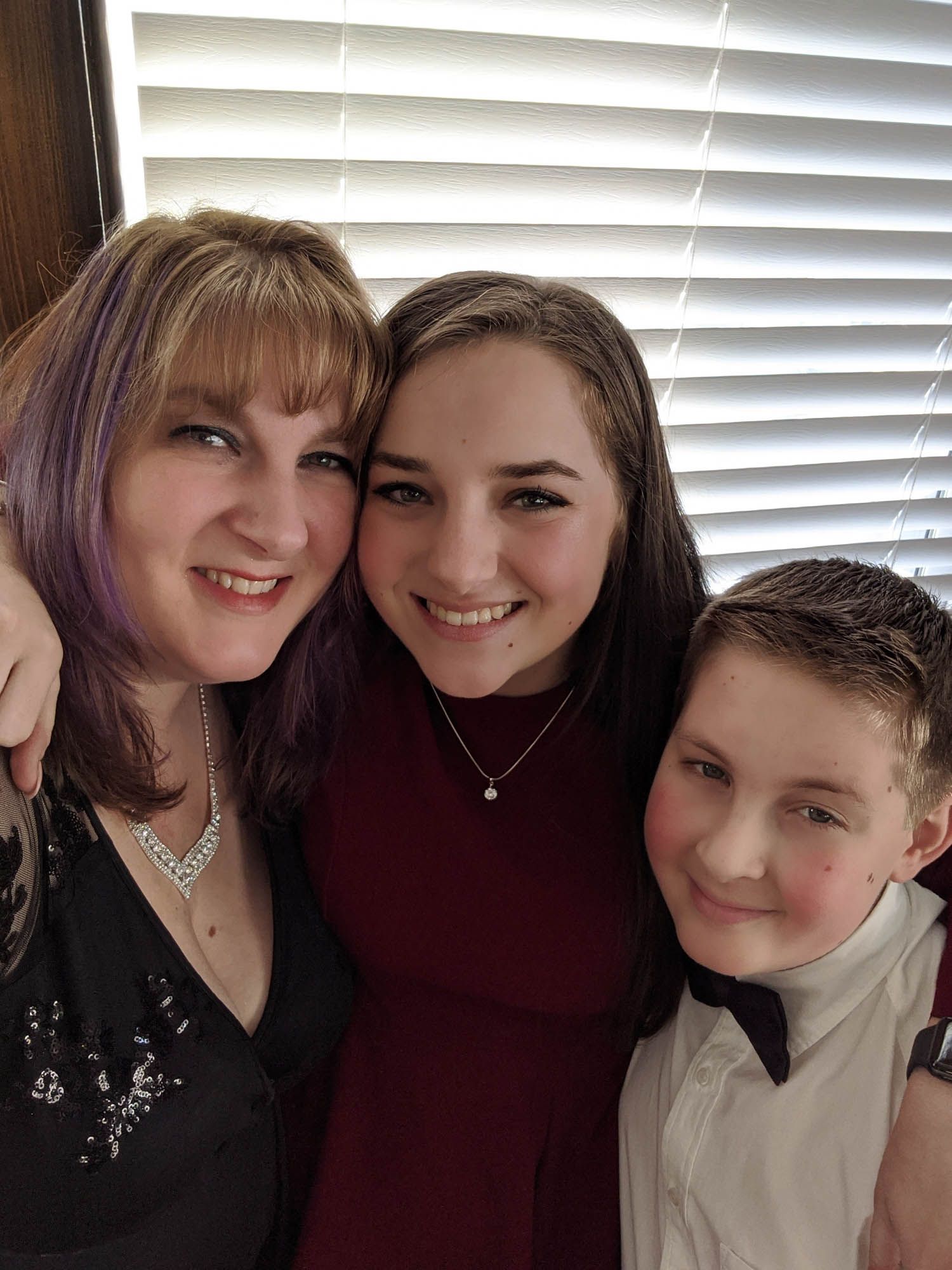 A woman with purple highlights poses with a teenage girl in burgundy and a young boy in a bow tie.