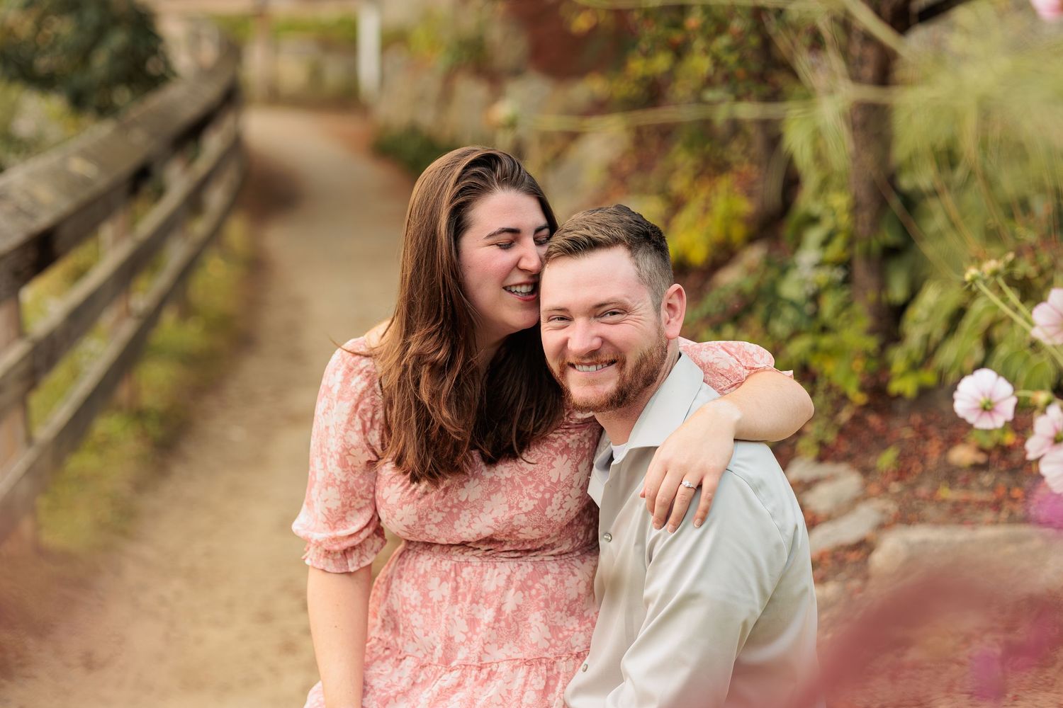 A laughing couple shares a joyful embrace on a garden path, the woman hugging the man from behind. Meredith Bay Meredith NH