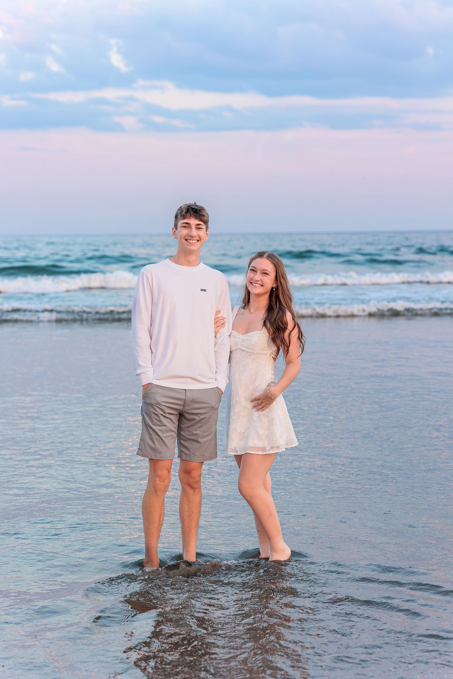 Young couple smiling and standing barefoot in ocean waves at sunset on a beautiful beach. Wells Reserve at Laudholm Wells ME