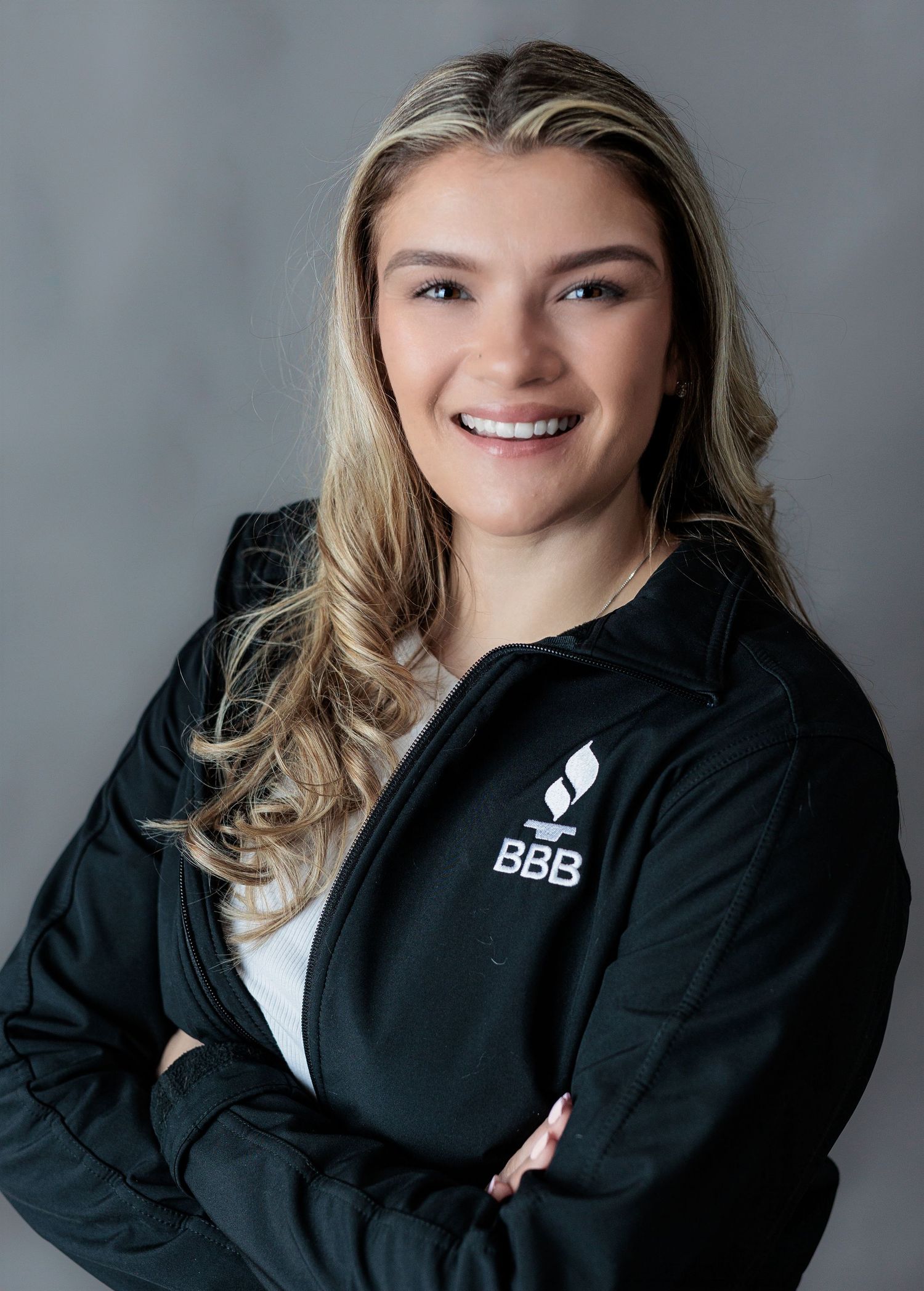 Young woman in BBB jacket smiling with arms crossed for professional headshot.