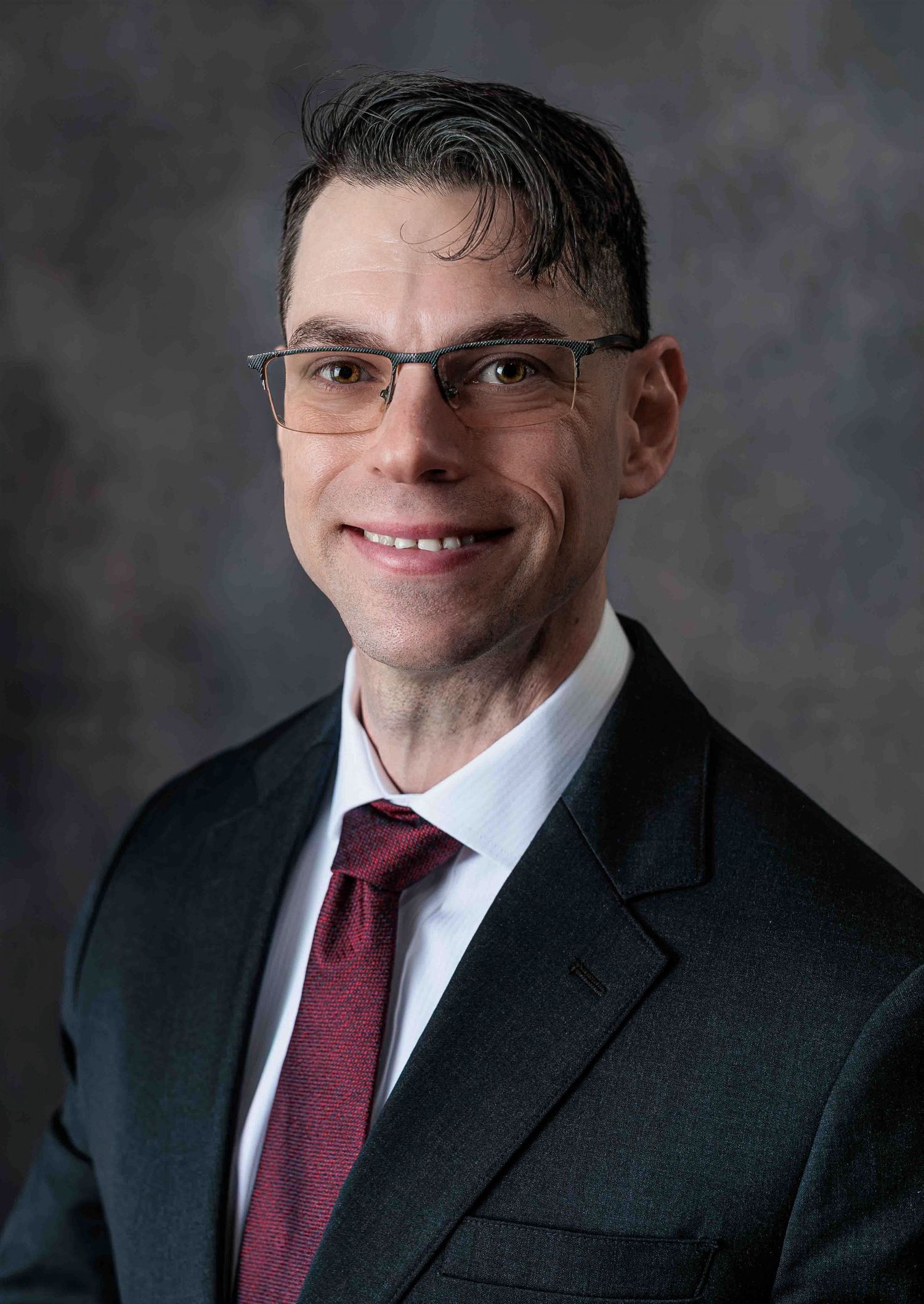 Professional man in dark suit and red tie smiling for corporate headshot.