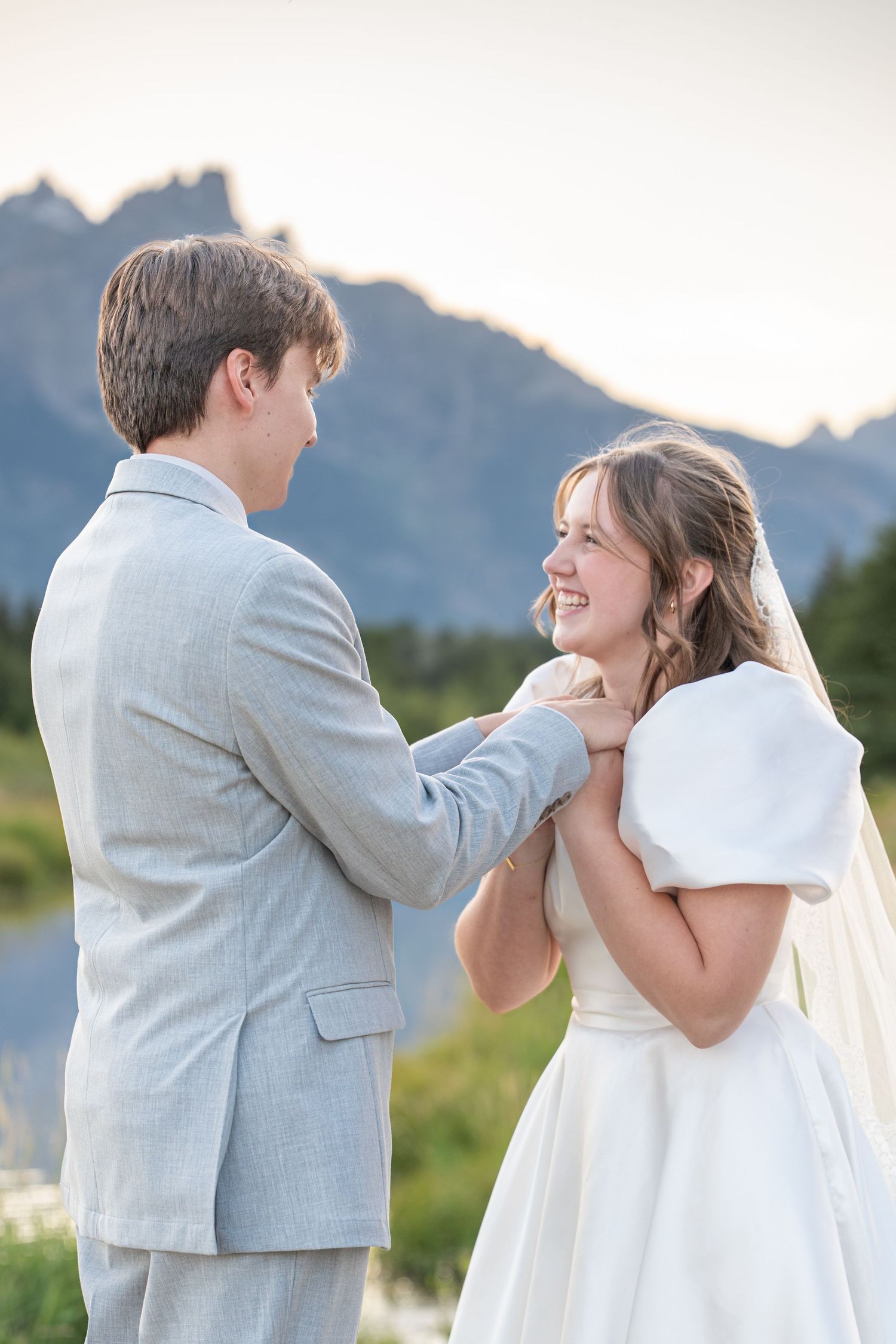 Joyful wedding couple laughing and embracing outdoors with mountains behind them.